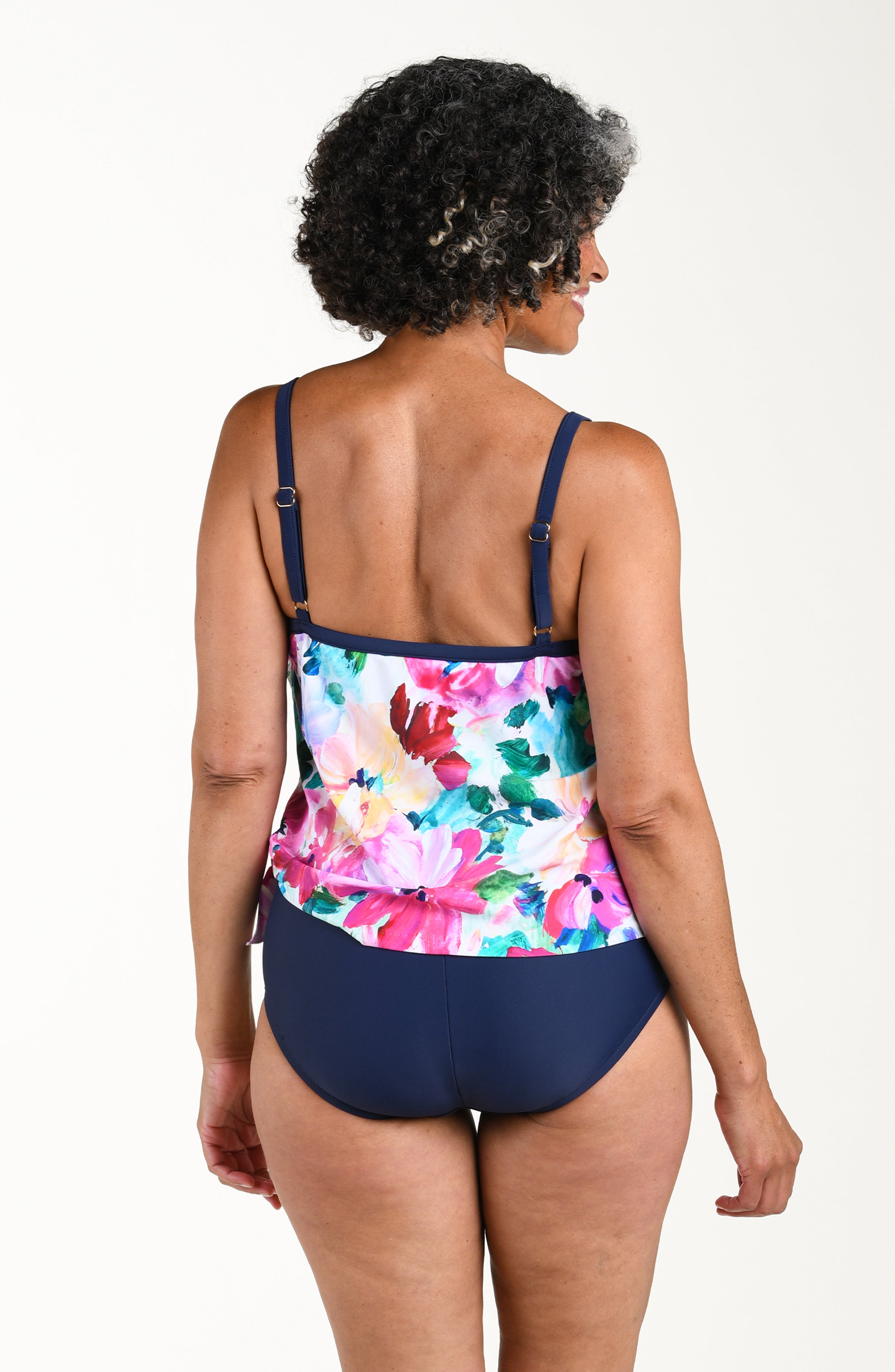 Woman wearing a colorful floral tankini top and navy shorts on a white background