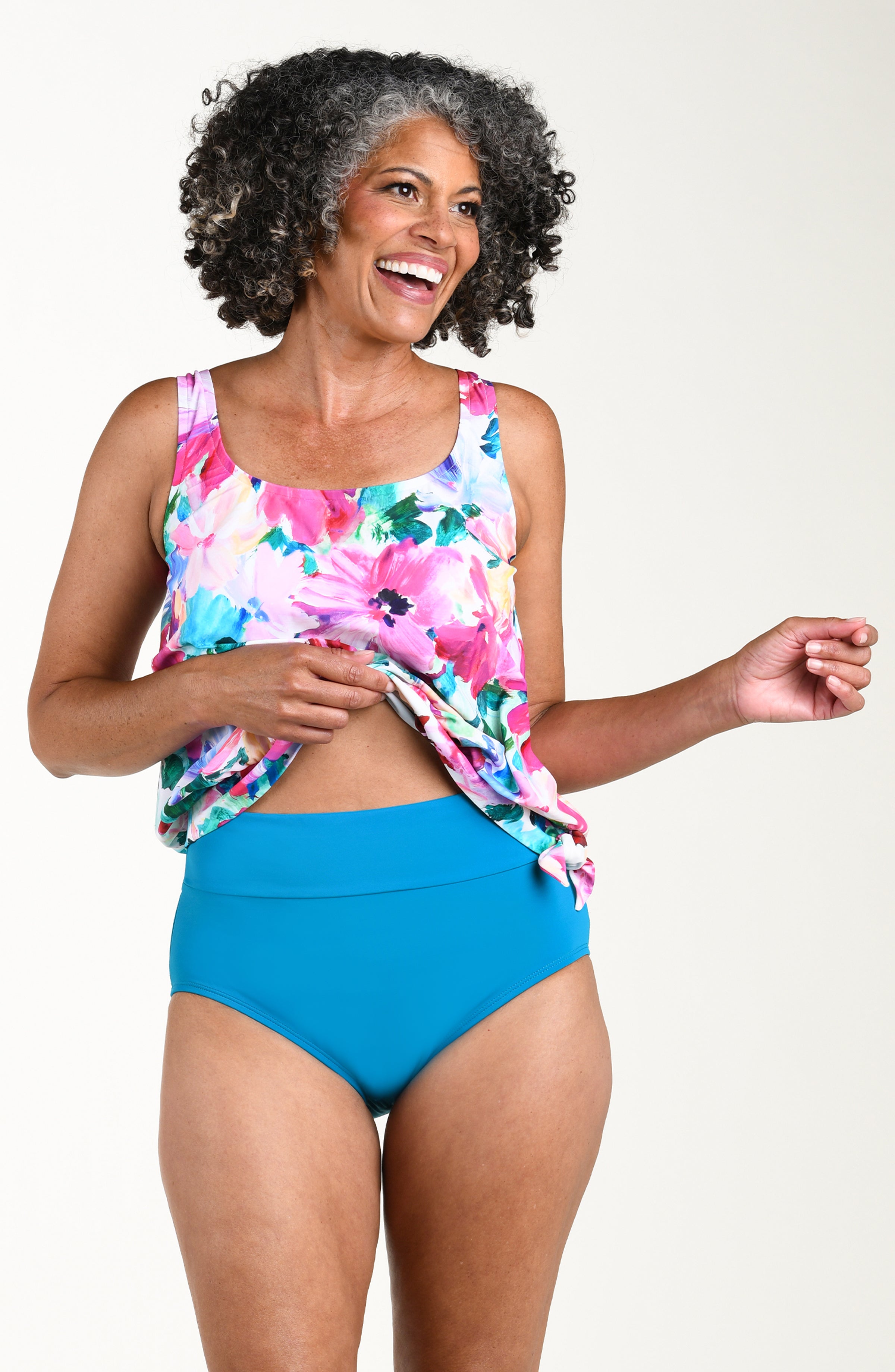Woman wearing a floral top and emerald colored high-waisted bikini bottoms on a white background