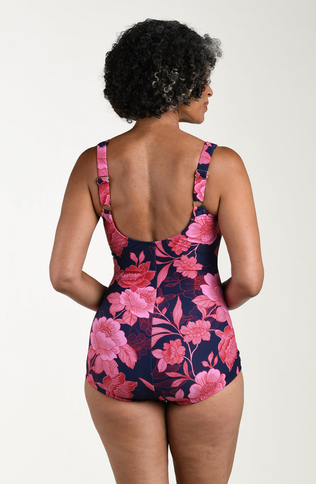 Back image of model wearing a multicolored (pink) floral printed one-piece swimsuit with wide straps, a scoop back, ruched body, and full rear coverage.