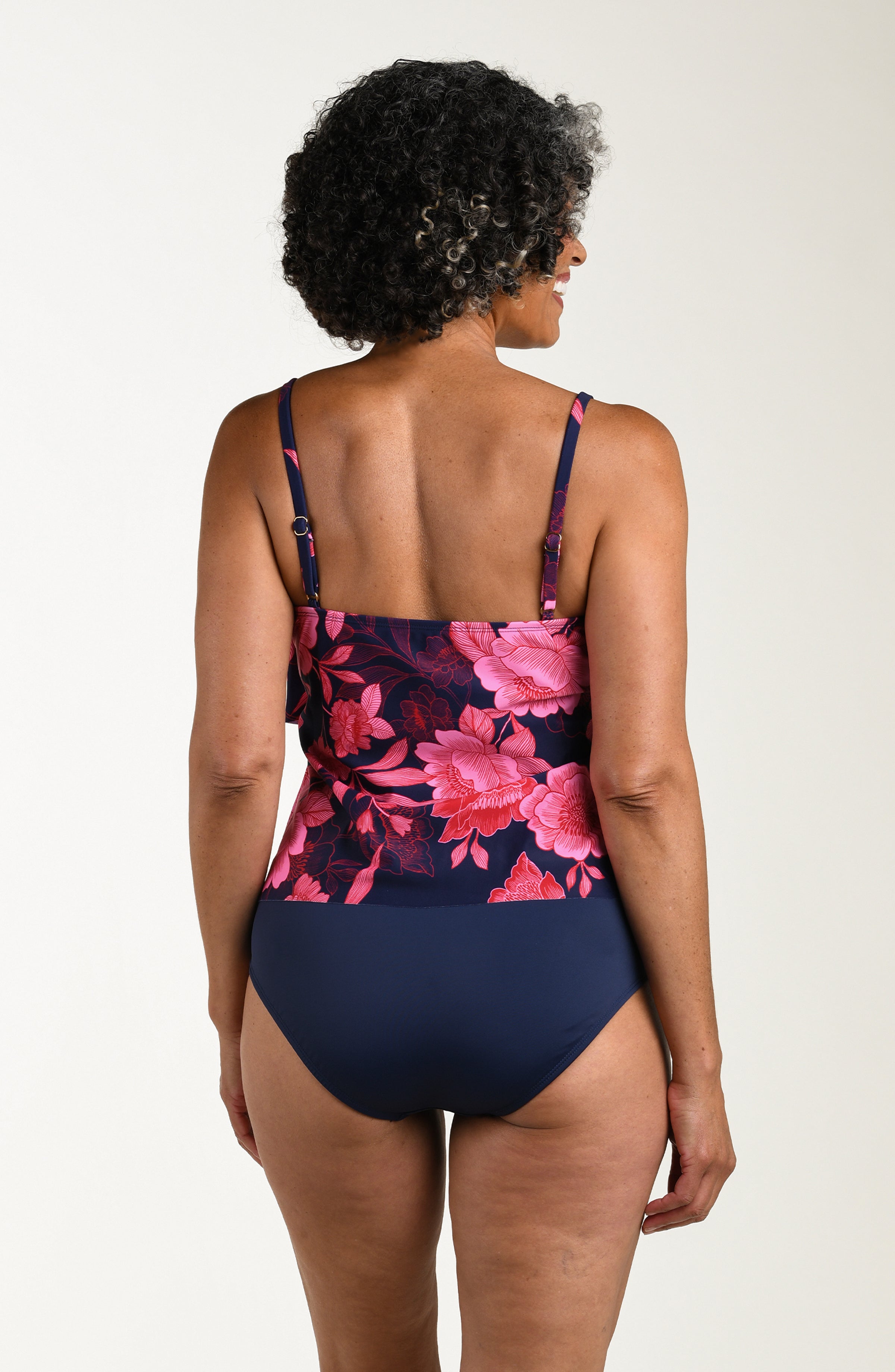 Back image of model wearing a multicolored (pink) floral printed tankini featuring thin over the shoulder straps and two tiers of ruffled layers.