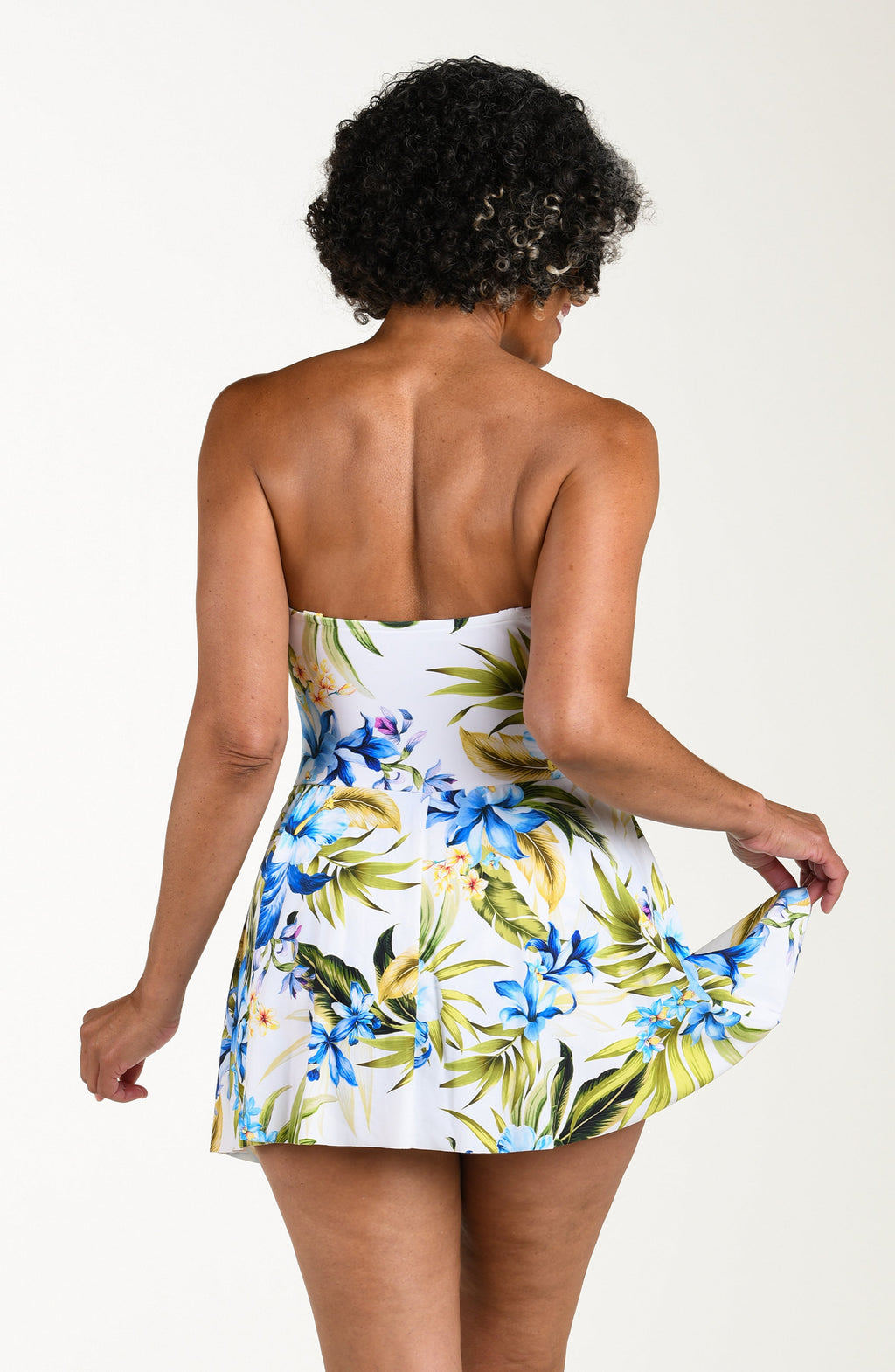 Back image of model wearing a multicolored (white) tropical one-piece swim dress featuring a sweetheart neckline, ruched bodice, removable straps, and a flared skirt.