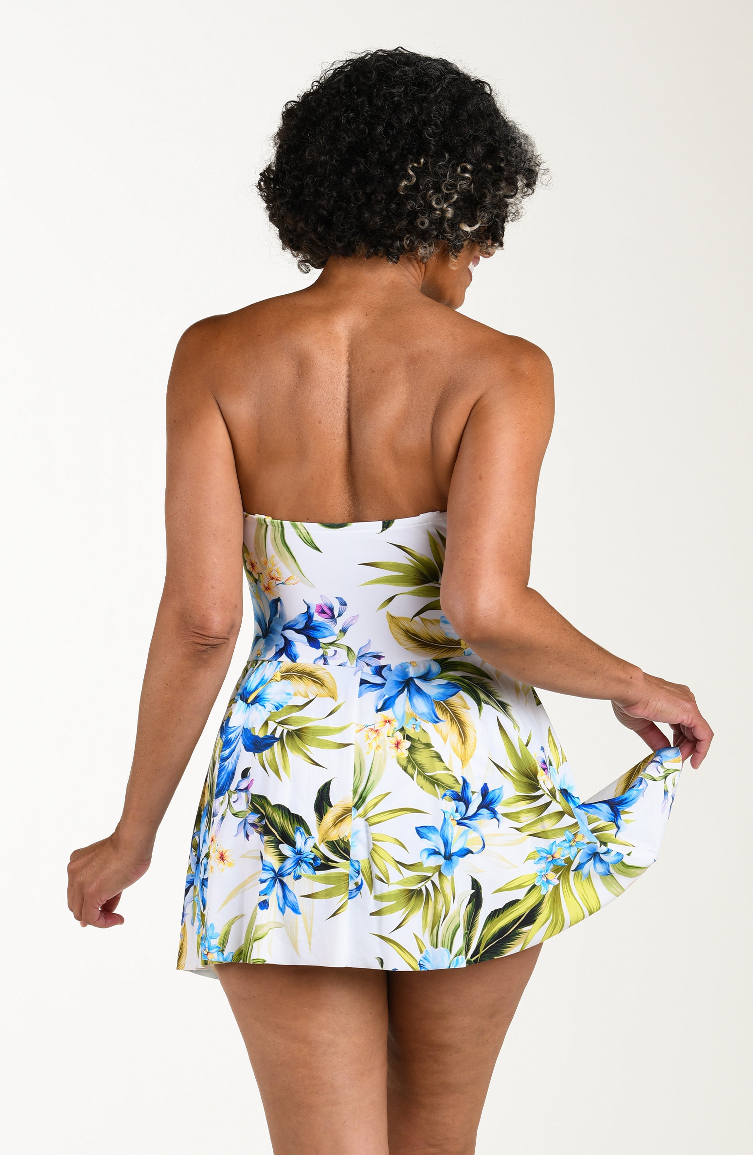 Back image of model wearing a multicolored (white) tropical one-piece swim dress featuring a sweetheart neckline, ruched bodice, removable straps, and a flared skirt.