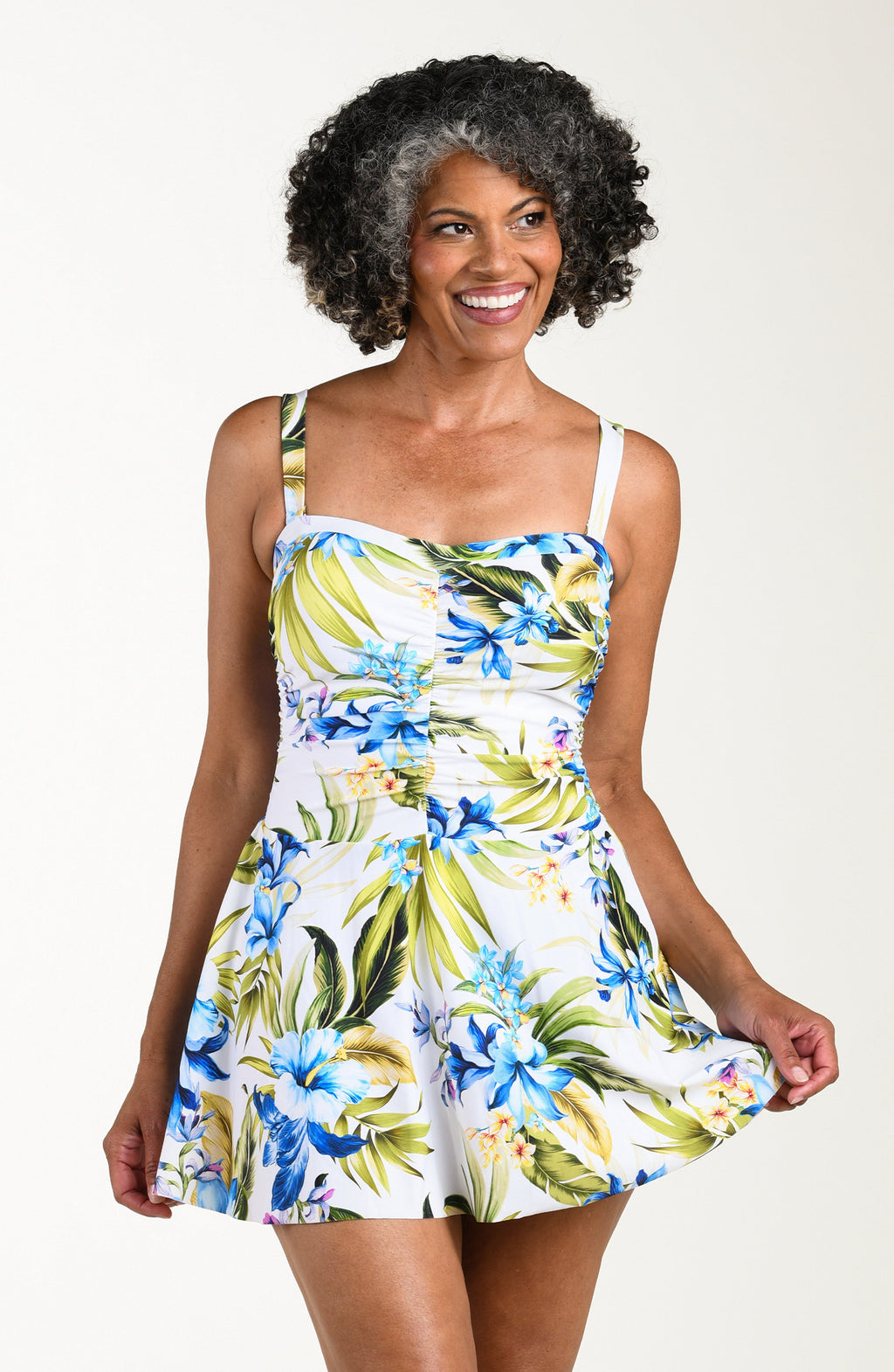 Front image of model wearing a multicolored (white) tropical one-piece swim dress featuring a sweetheart neckline, ruched bodice, removable straps, and a flared skirt.