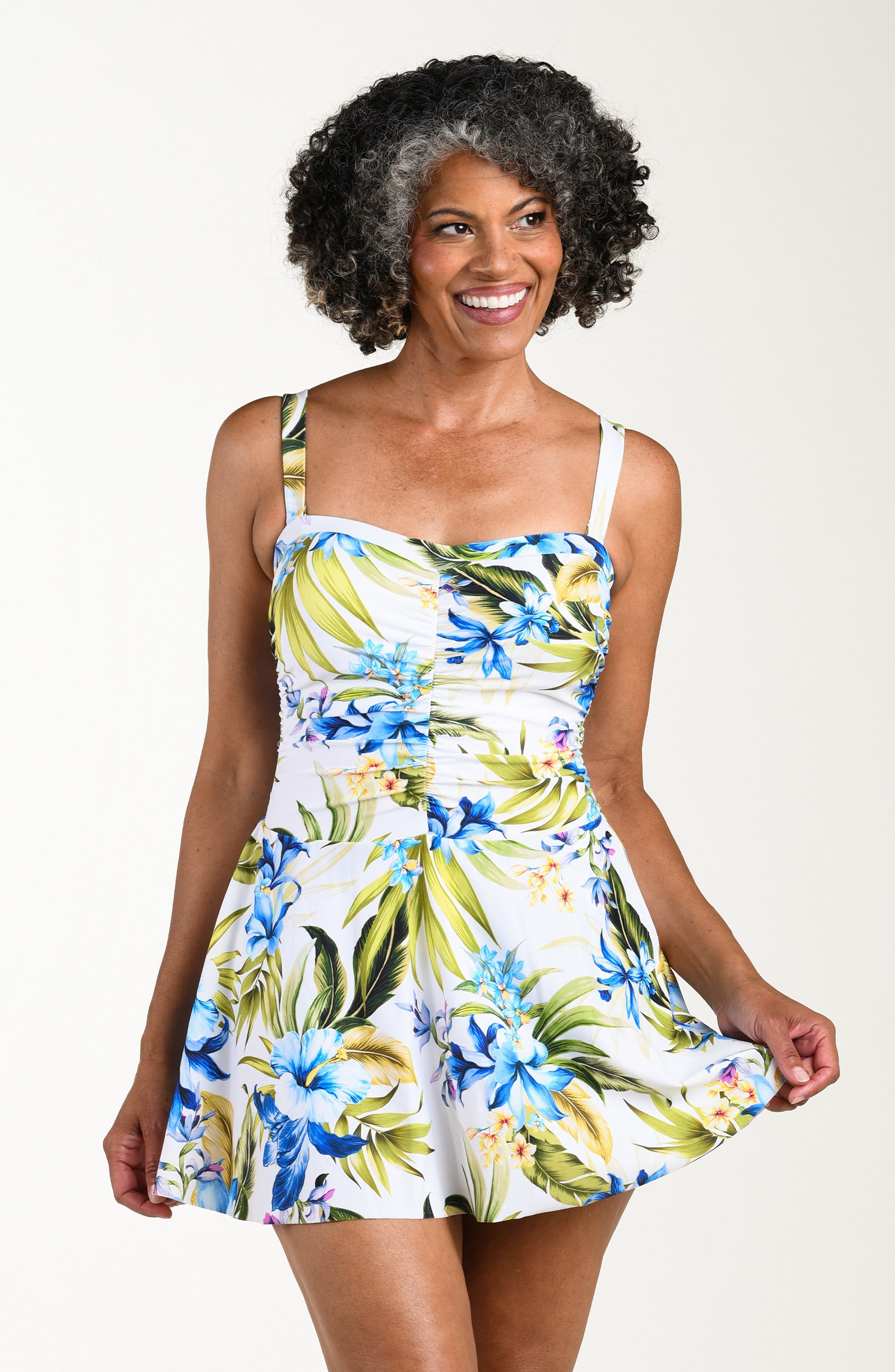 Front image of model wearing a multicolored (white) tropical one-piece swim dress featuring a sweetheart neckline, ruched bodice, removable straps, and a flared skirt.