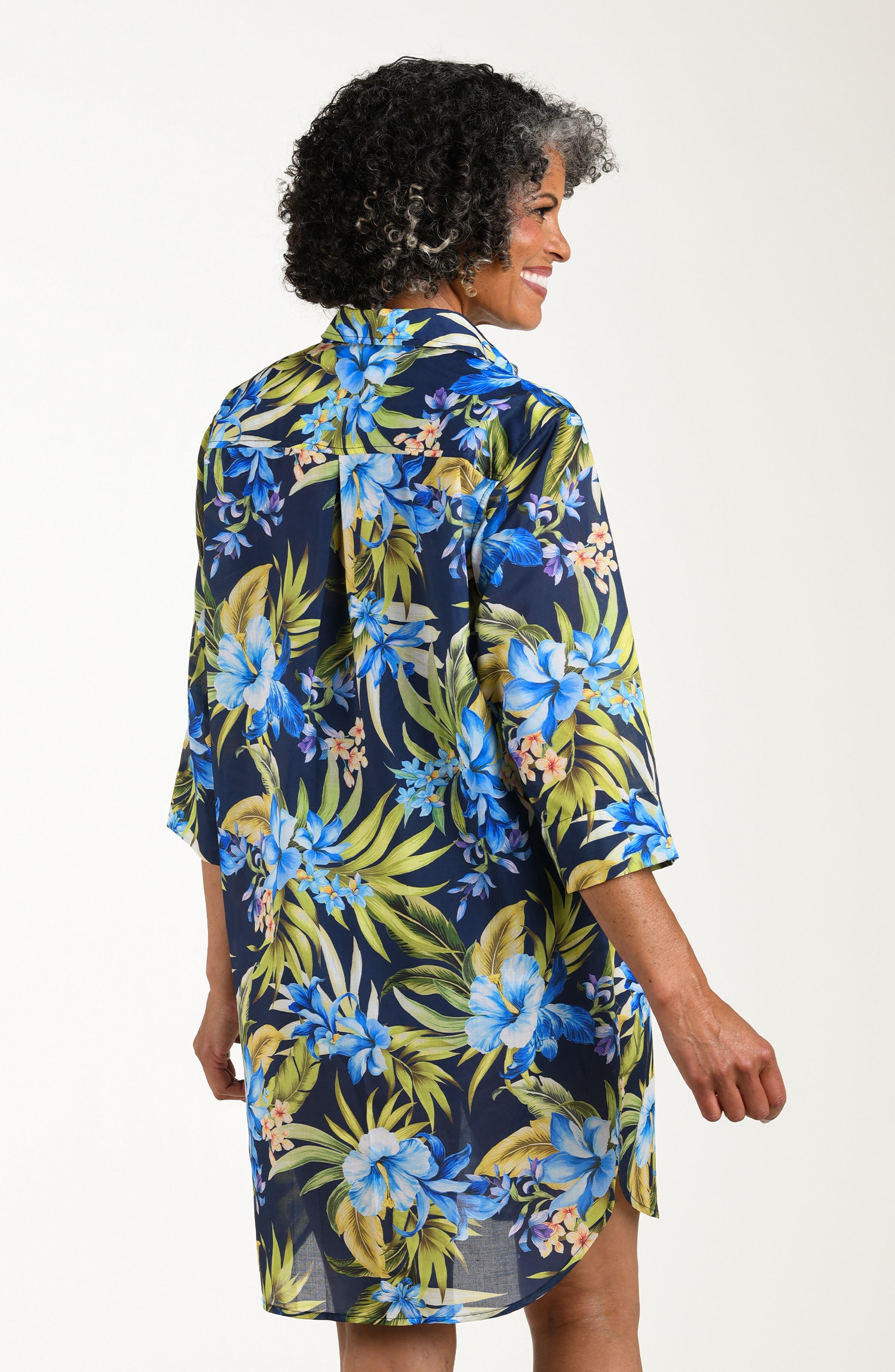 Back image of model wearing a multicolored (blue) tropical tunic cover up featuring a collared button front and three quarter sleeves. 