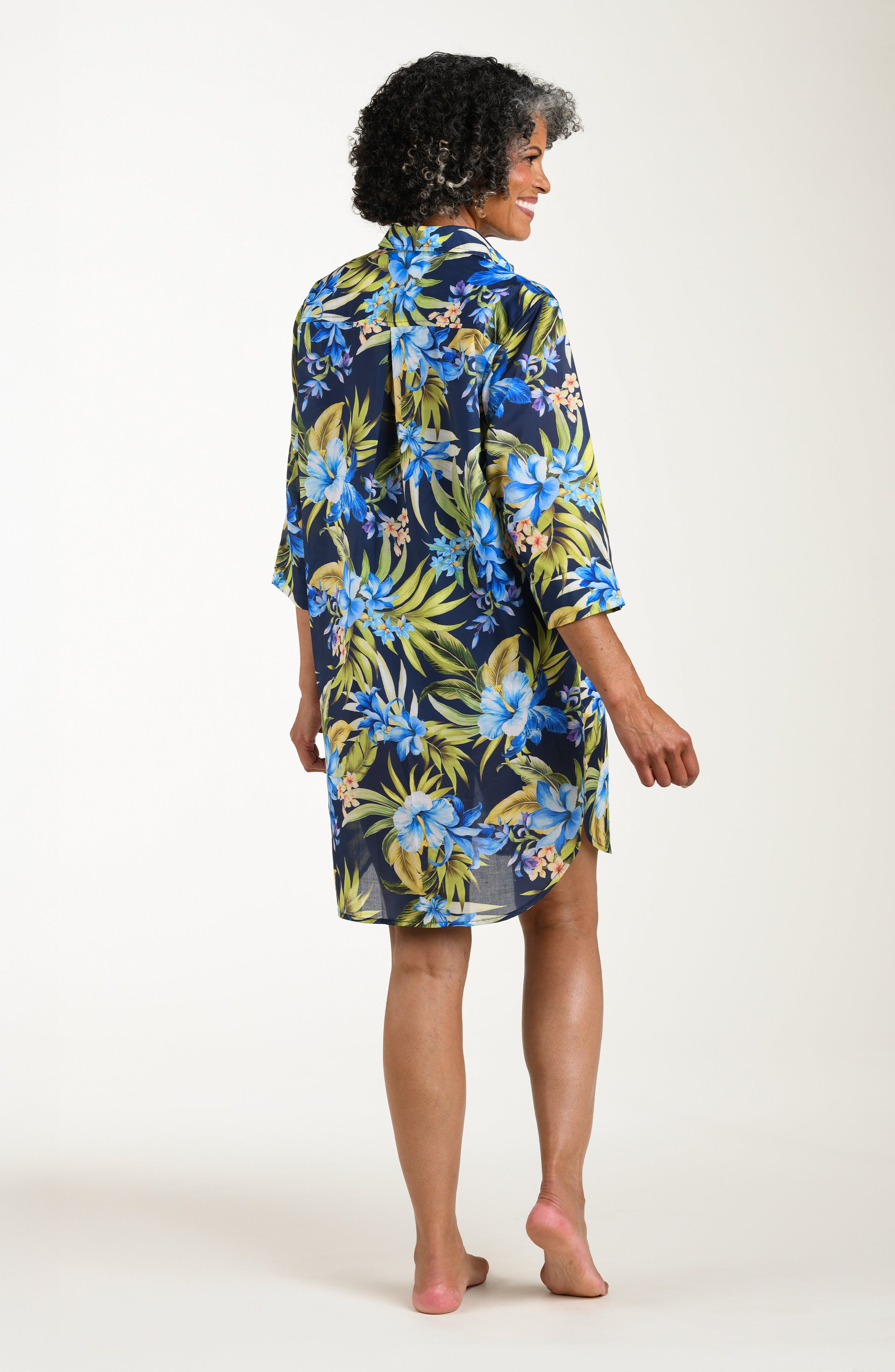 Back image of model wearing a multicolored (blue) tropical tunic cover up featuring a collared button front and three quarter sleeves. 