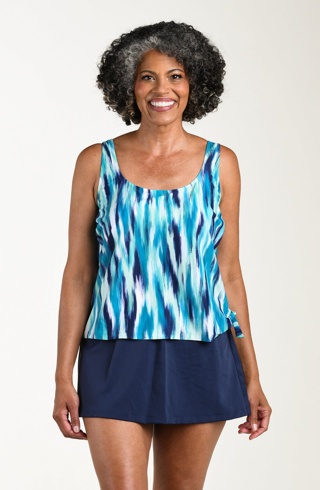 Front image of model wearing a multicolored teal colored one-piece featuring a scoop neckline, over the shoulder straps, and side tie detail. The top looks like a tankini and the bottom is solid indigo skirt.