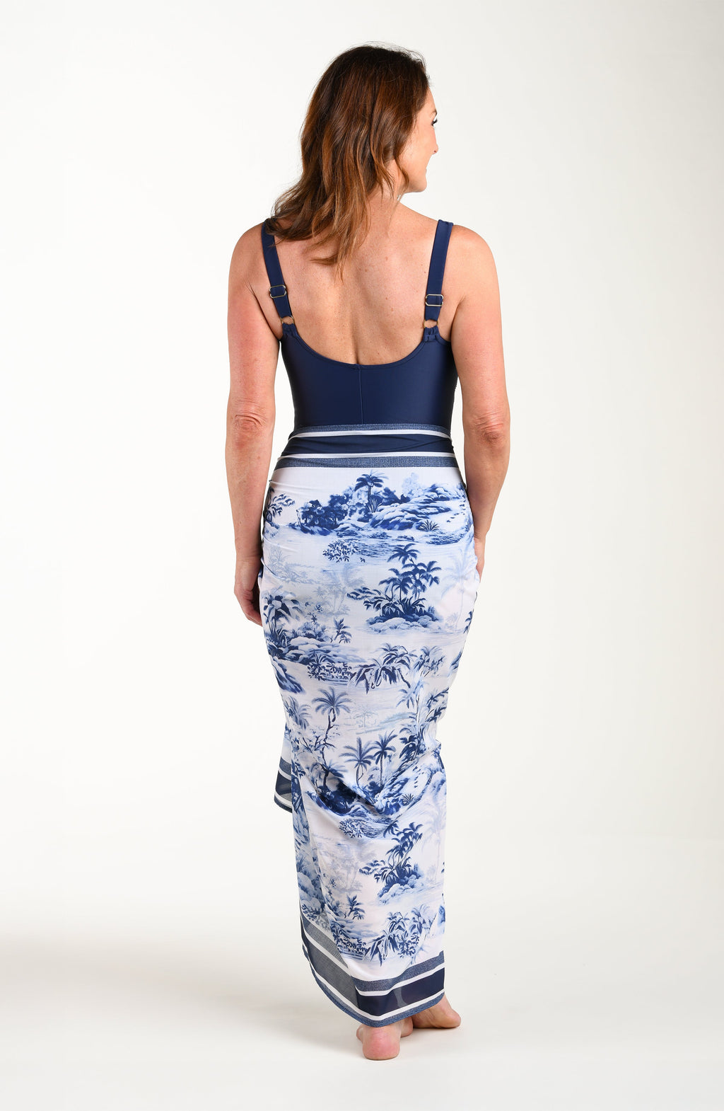 Full body back image of model wearing a multicolored white and blue tropical pareo which is tied to the side. 