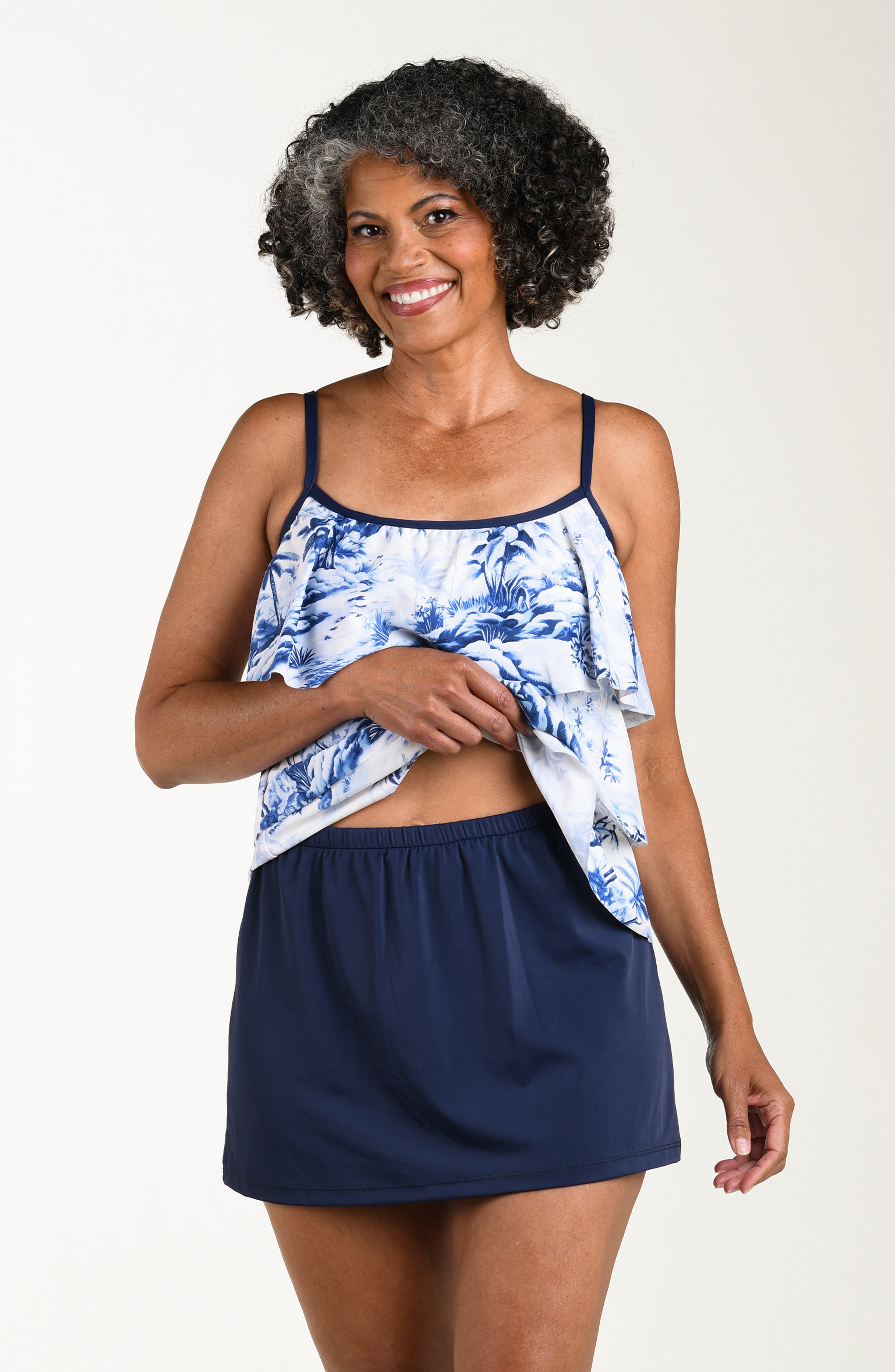 Front image of model wearing a multicolored white and blue tropical tankini featuring thin over the shoulder straps and three tiered ruffled layers. 