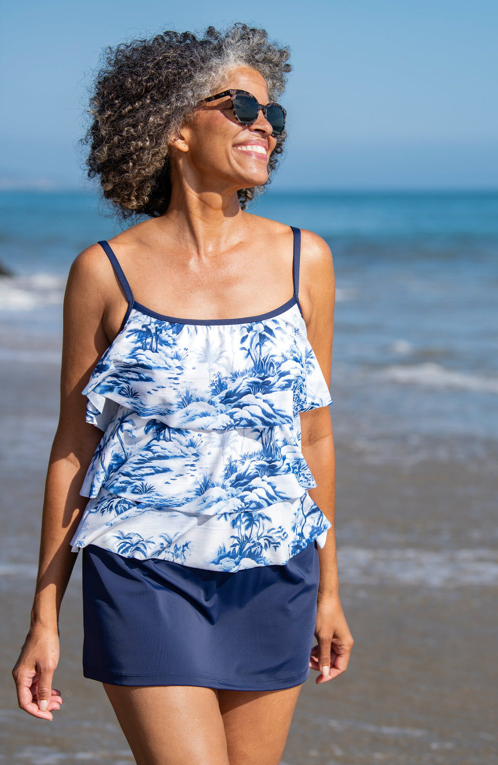 Woman wearing a blue and white floral top and navy shorts on a beach.