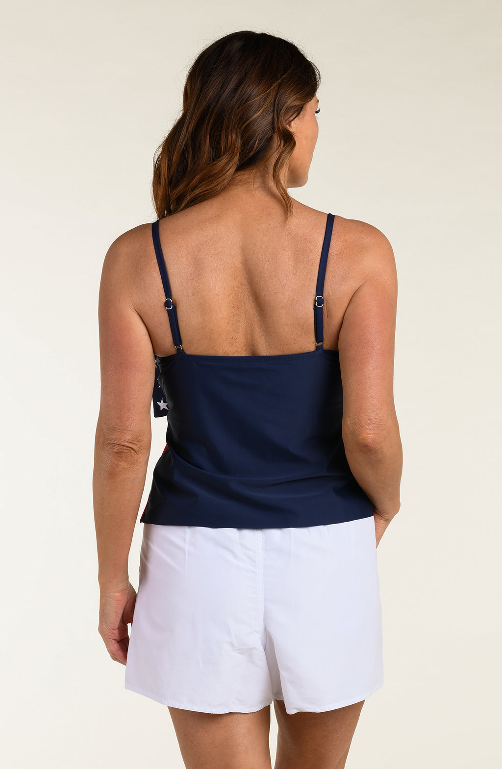 Woman wearing a tankini top with American flag design and white board shorts against a plain background