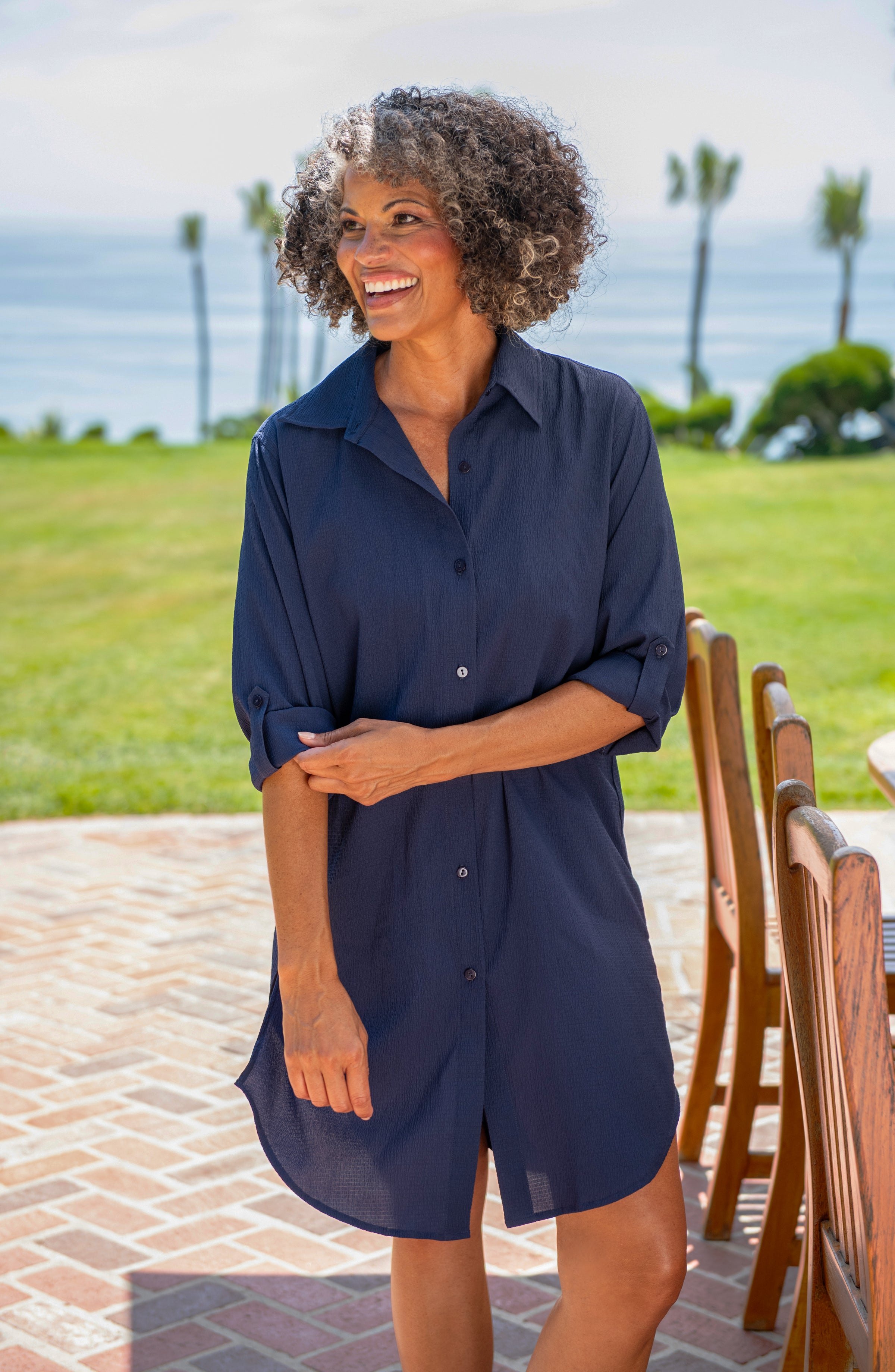 Woman wearing a navy blue dress standing outdoors with palm trees and grass in the background