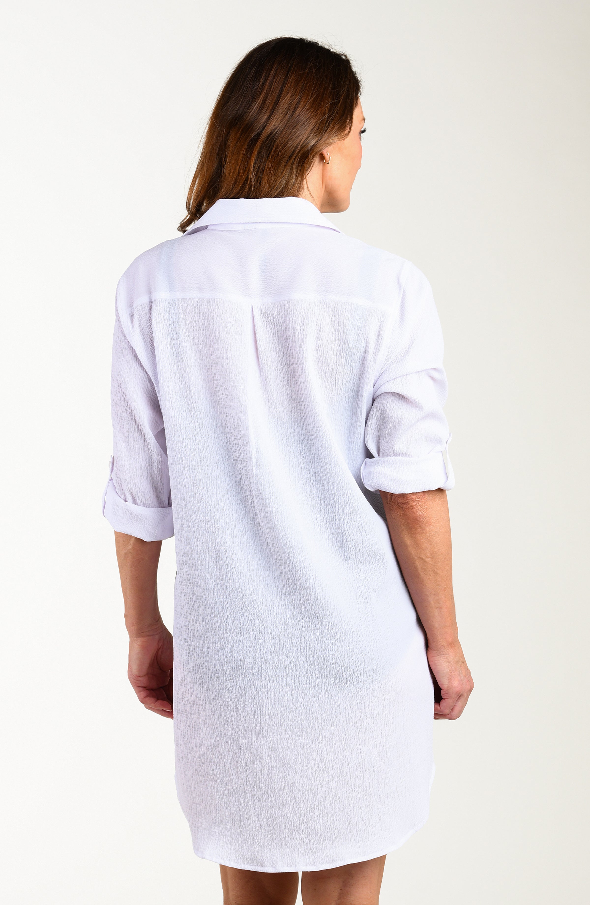 Back image of model wearing a solid white colored button-down swimsuit cover-up with a collared neckline, rolled 3/4 sleeves, and a mid-thigh length.