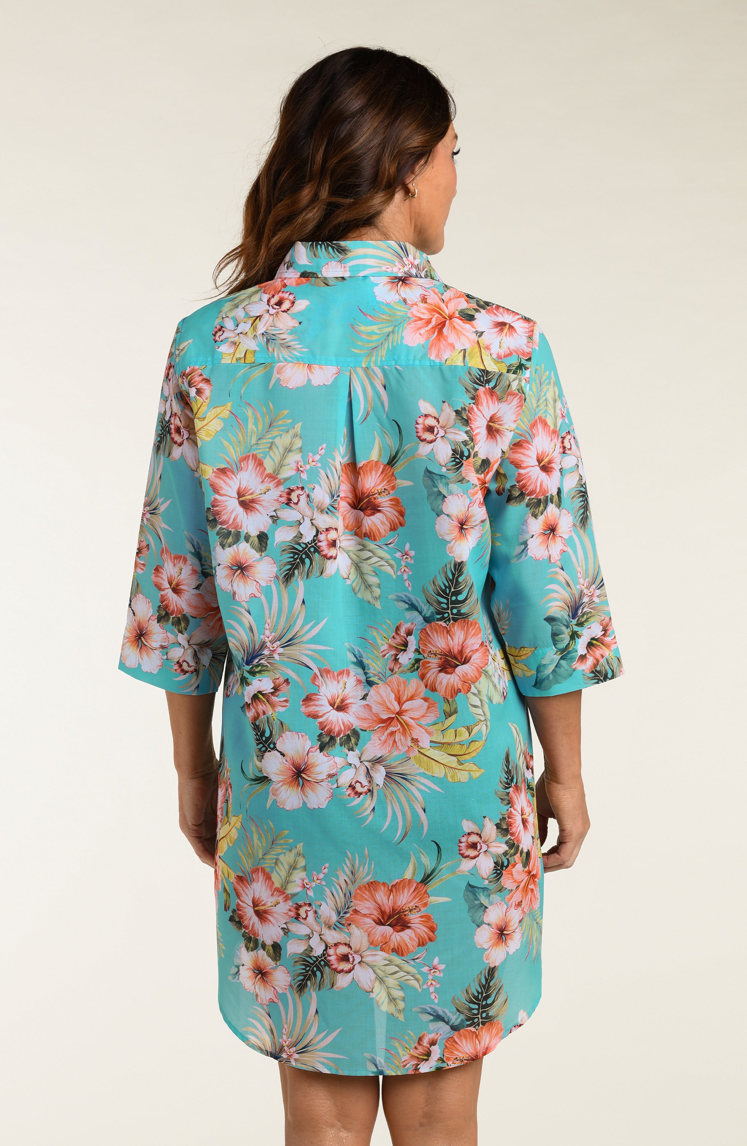 Woman wearing a floral button up cover up shirt against a plain background