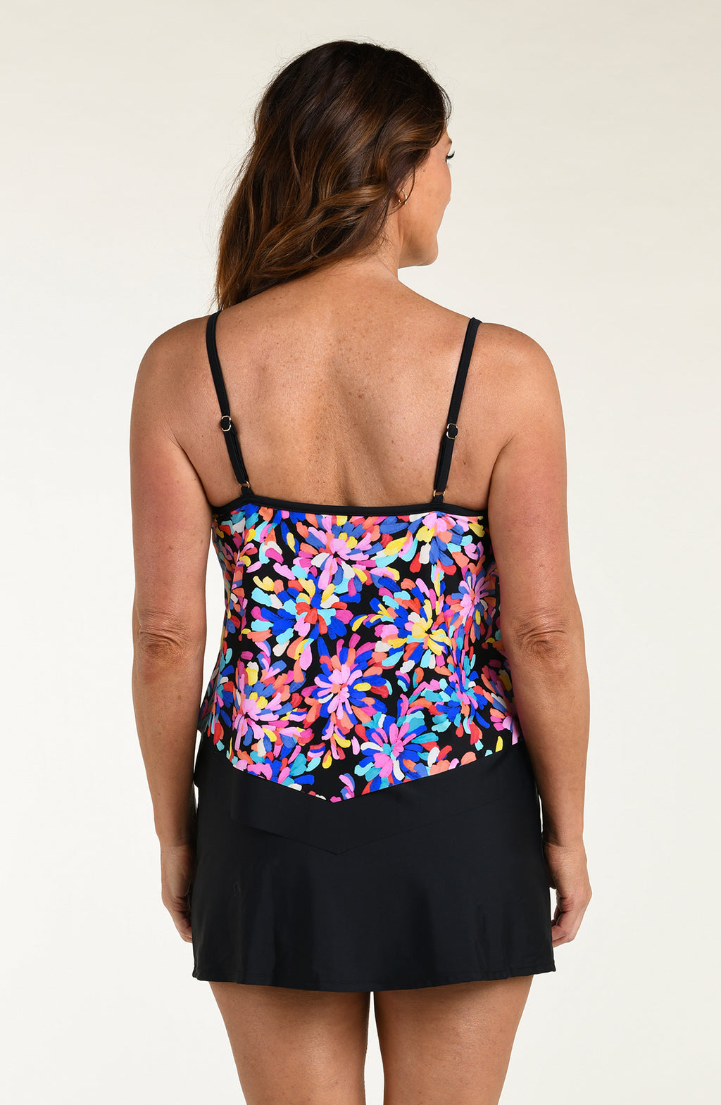 Woman wearing a colorful floral tankini top and black swim skirt on a white background