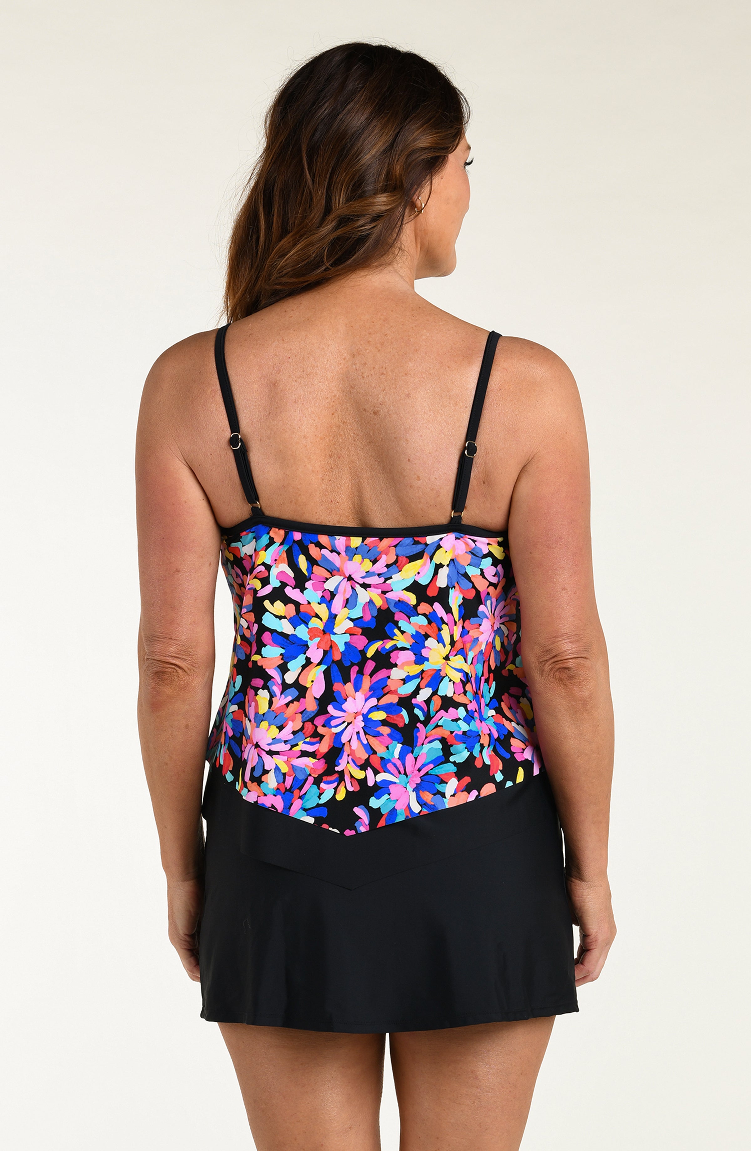 Woman wearing a colorful floral tankini top and black swim skirt on a white background