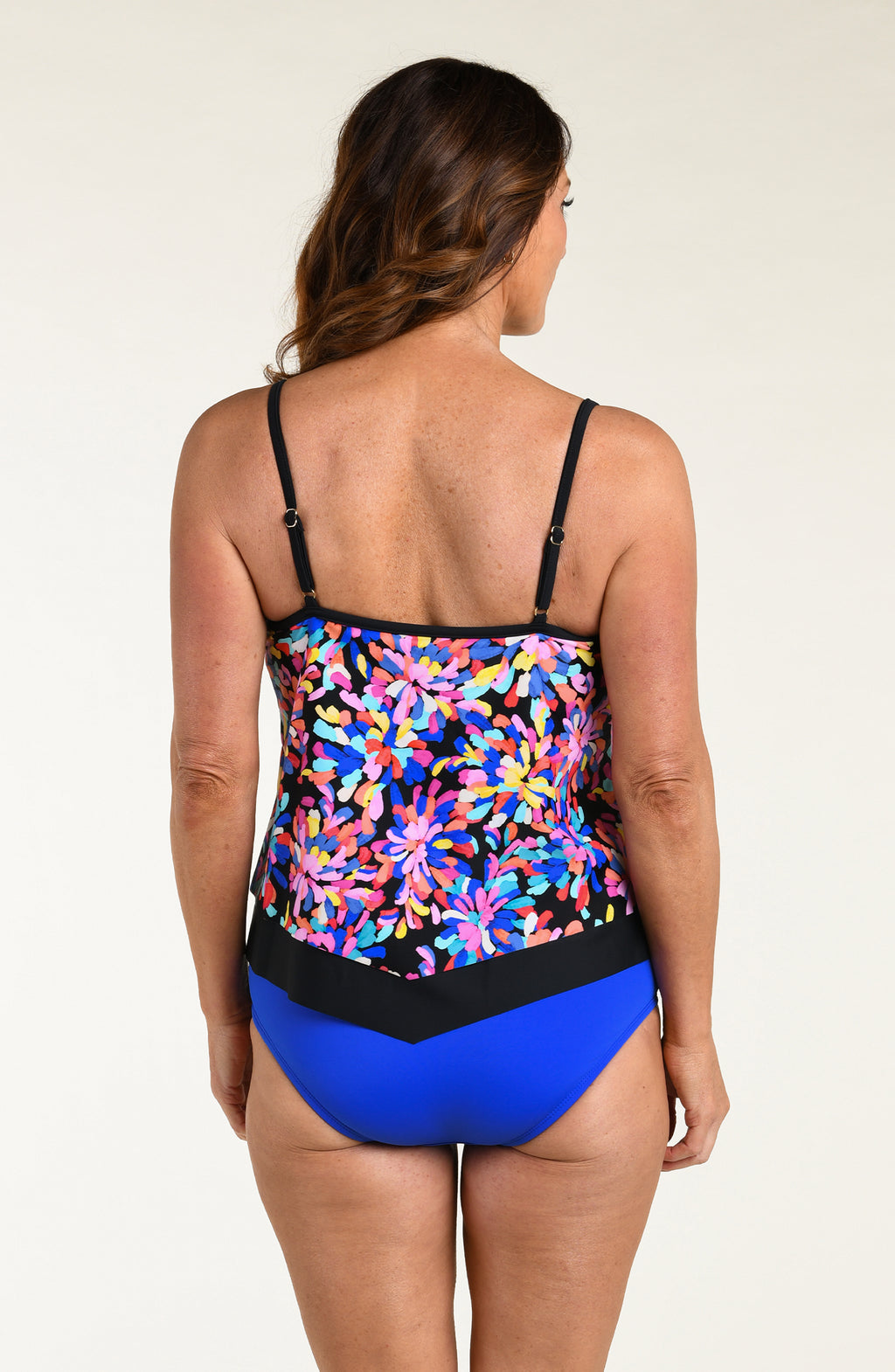 Woman wearing a colorful floral tankini top and blue swim bottoms on a white background