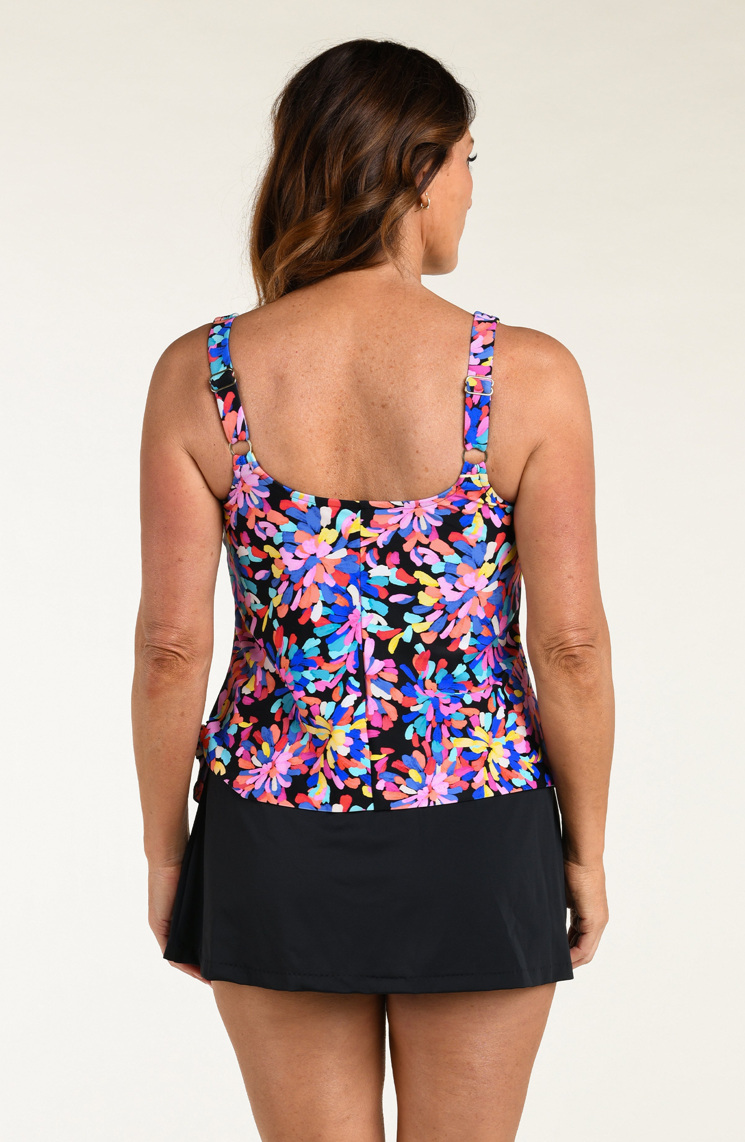 Woman wearing a colorful floral tankini top and black swim skirt on a beige background