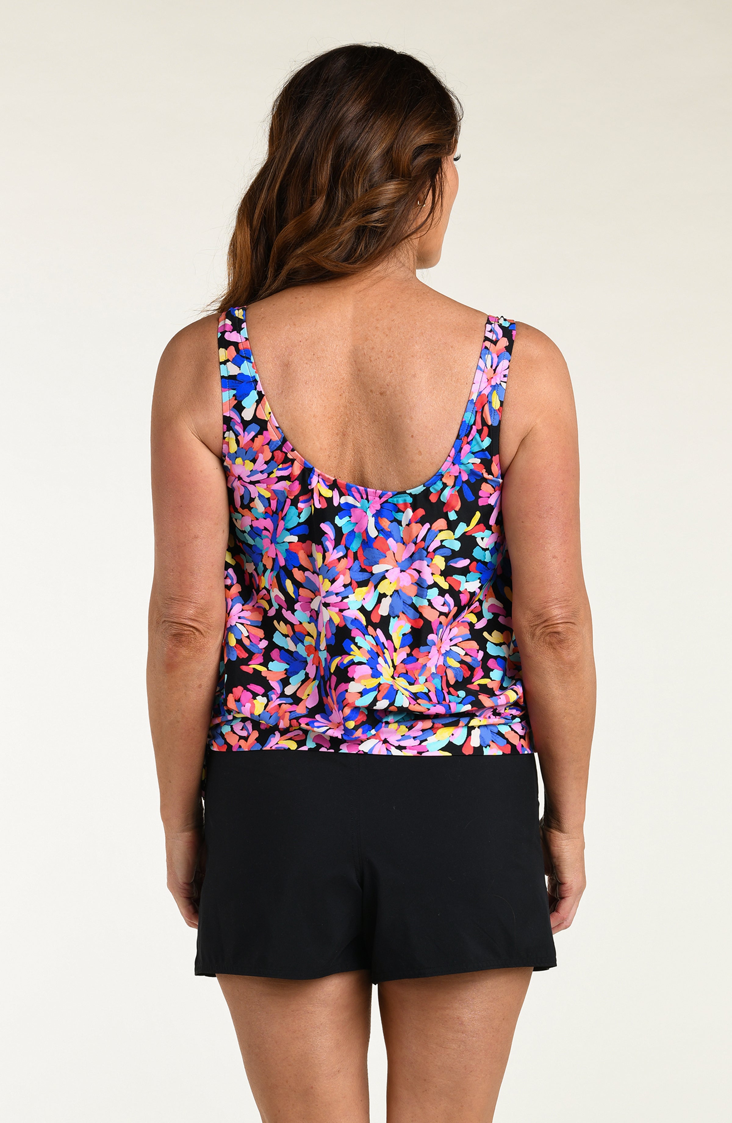 Woman wearing a colorful floral tankini top and black swim shorts on a plain background