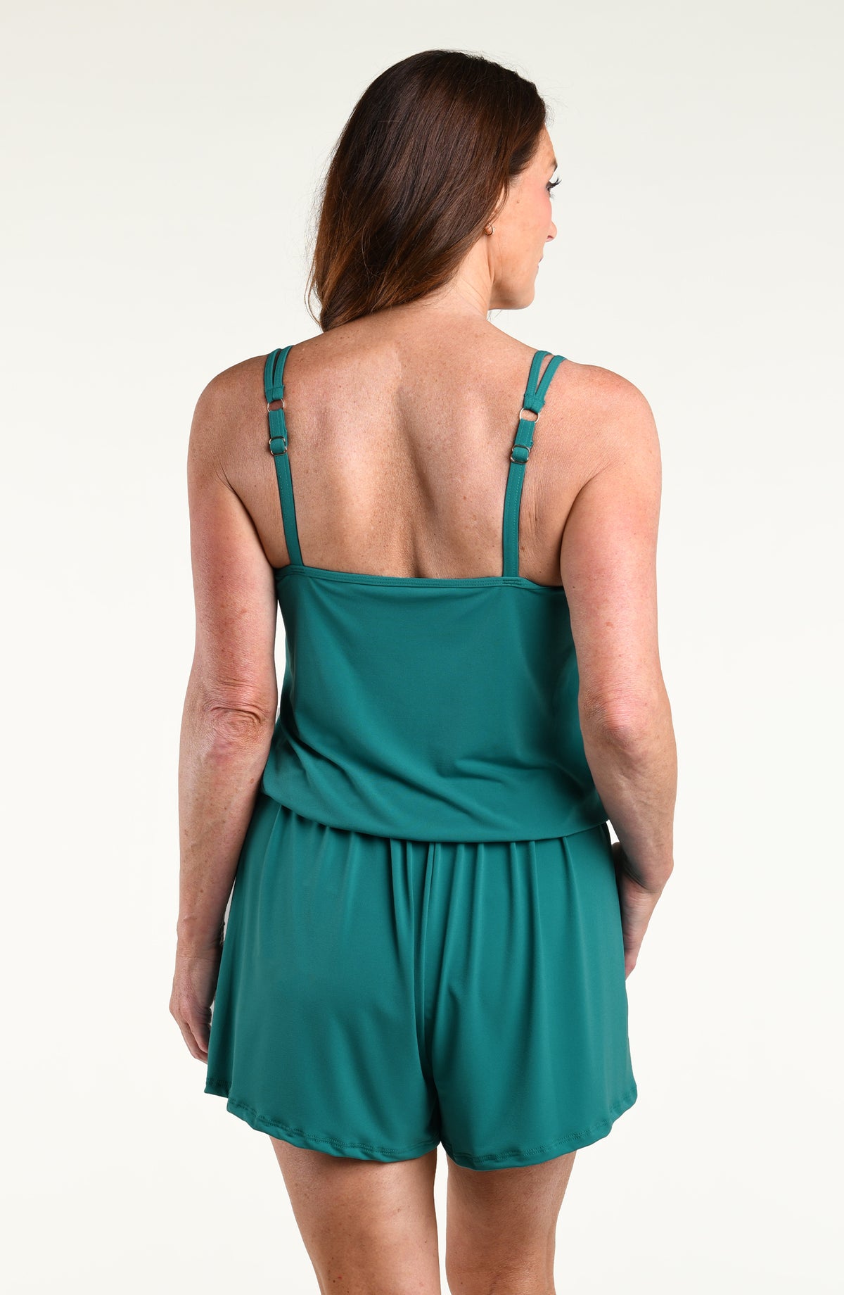 A woman modeling a teal green sleeveless romper with a ruffled peplum waist and matching shorts, set against a plain white studio background.