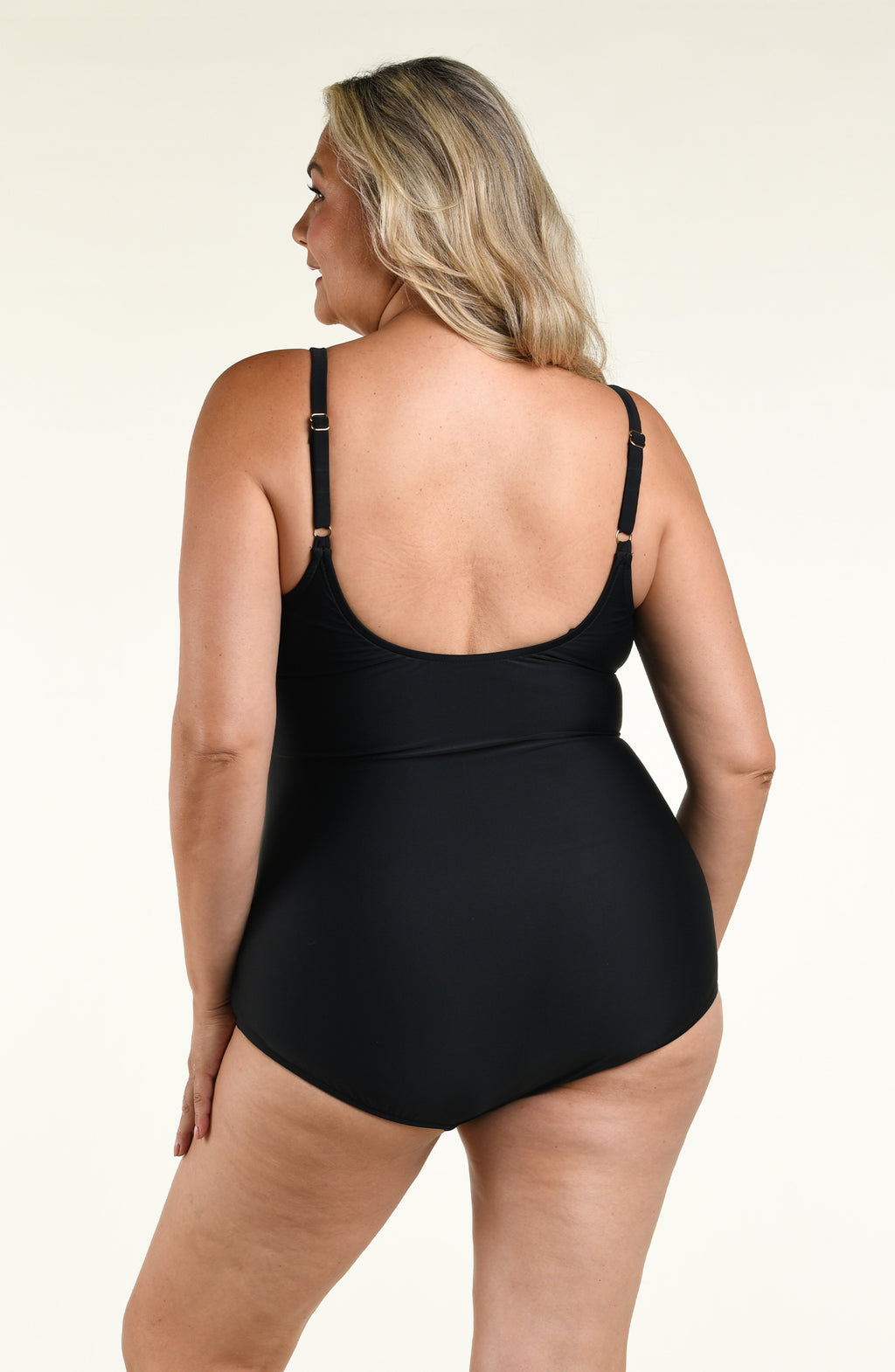 Woman wearing a solid black one piece swimsuit against a white background. 
