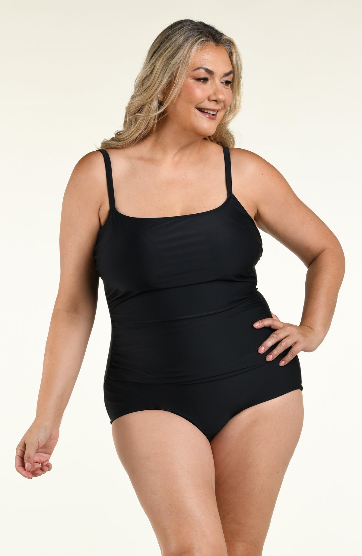 Woman wearing a solid black one piece swimsuit against a white background. 