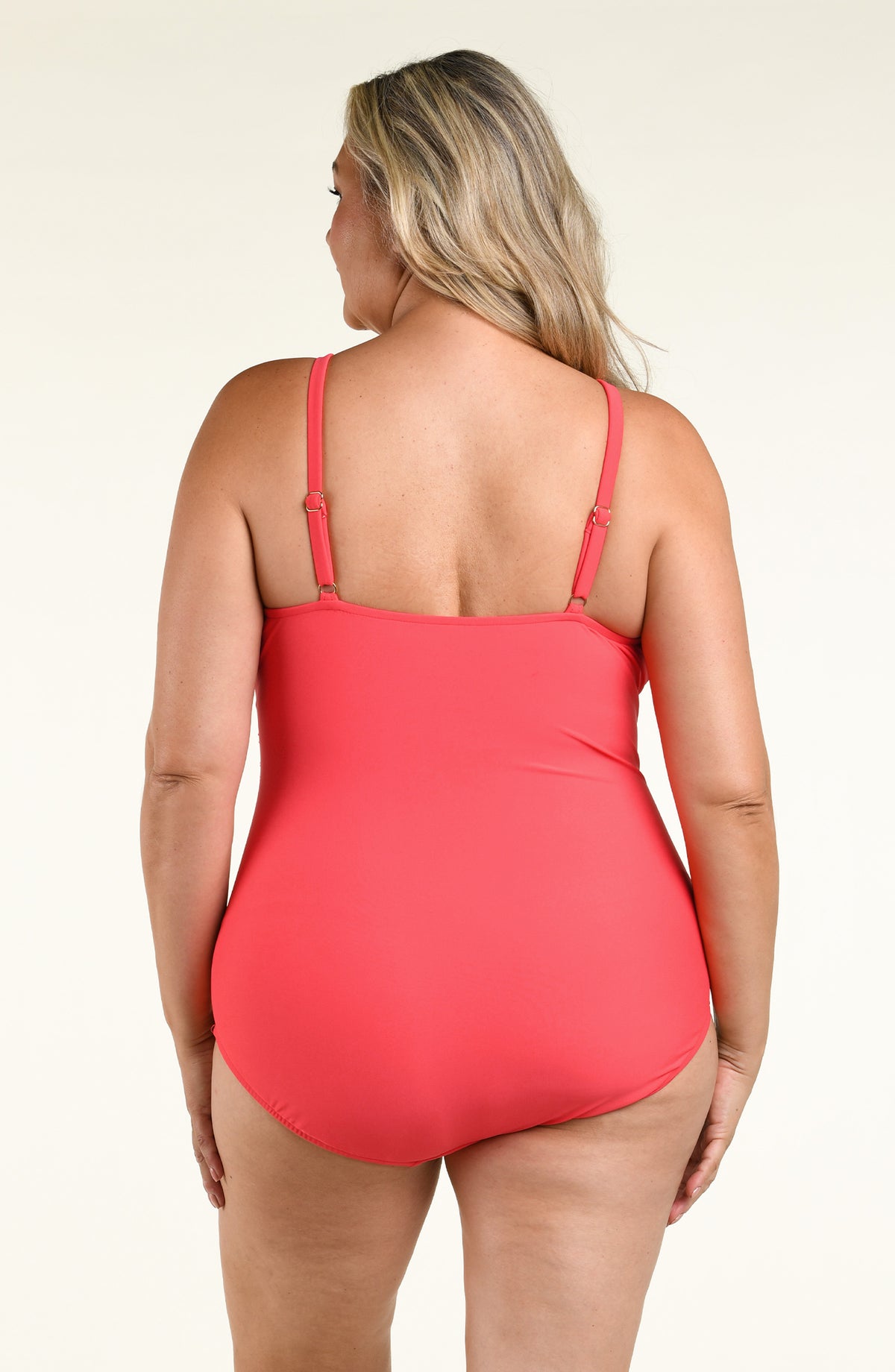 A woman modeling a coral red halter-neck one-piece swimsuit against a plain white studio background.