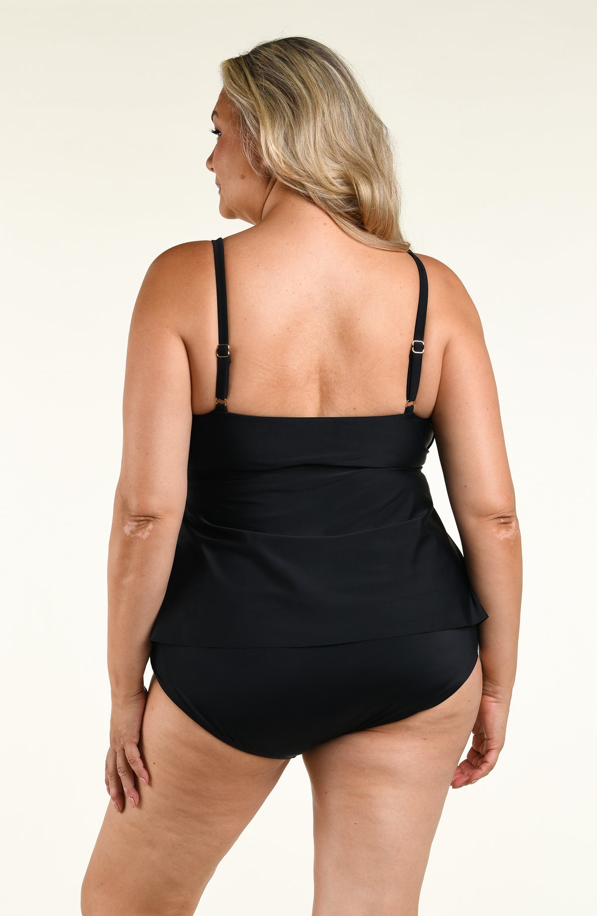 Woman wearing a solid black double tiered tankini top and matching bottom against a white background. 