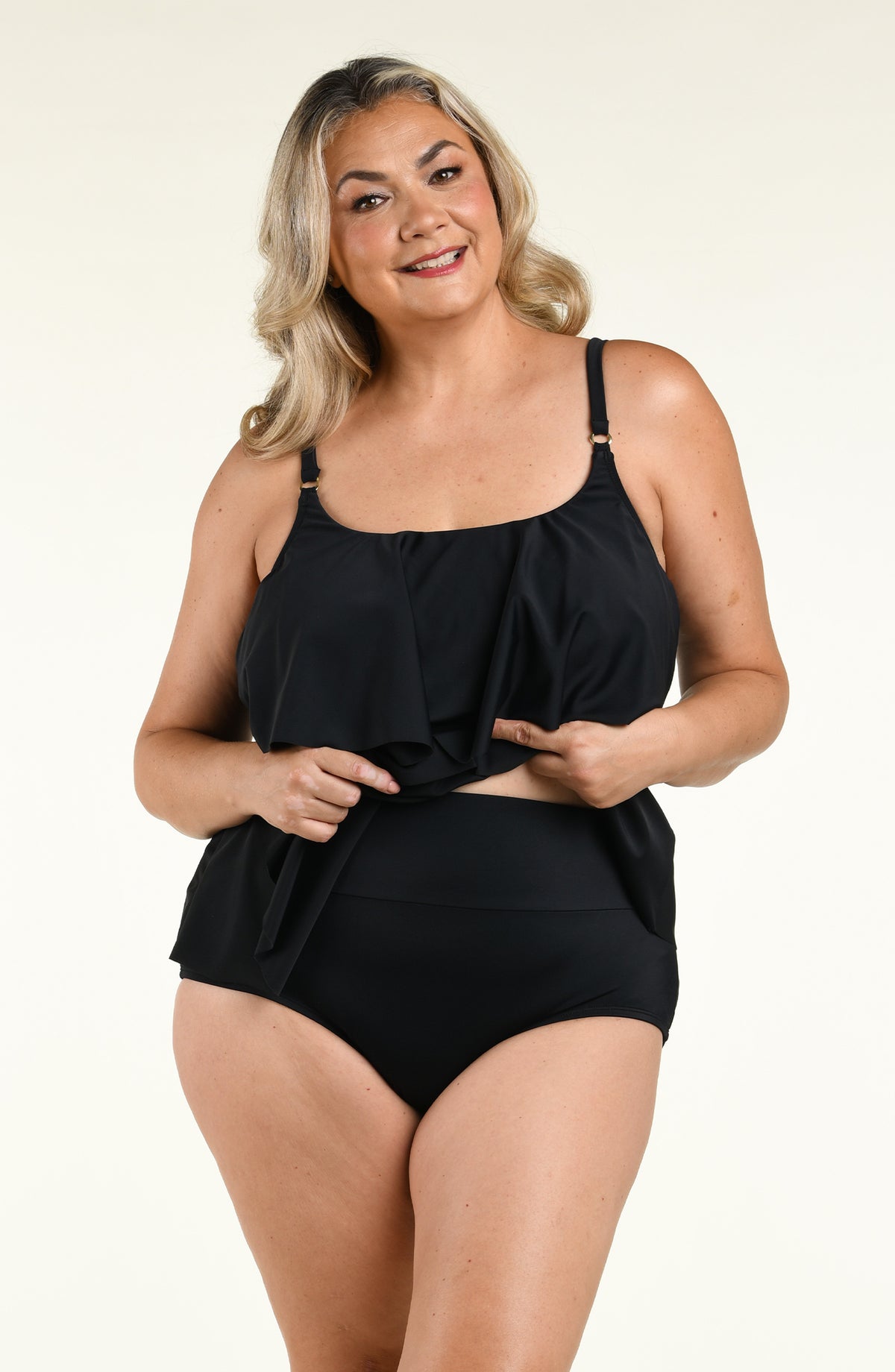 Woman wearing a solid black double tiered tankini top and matching bottom against a white background. 