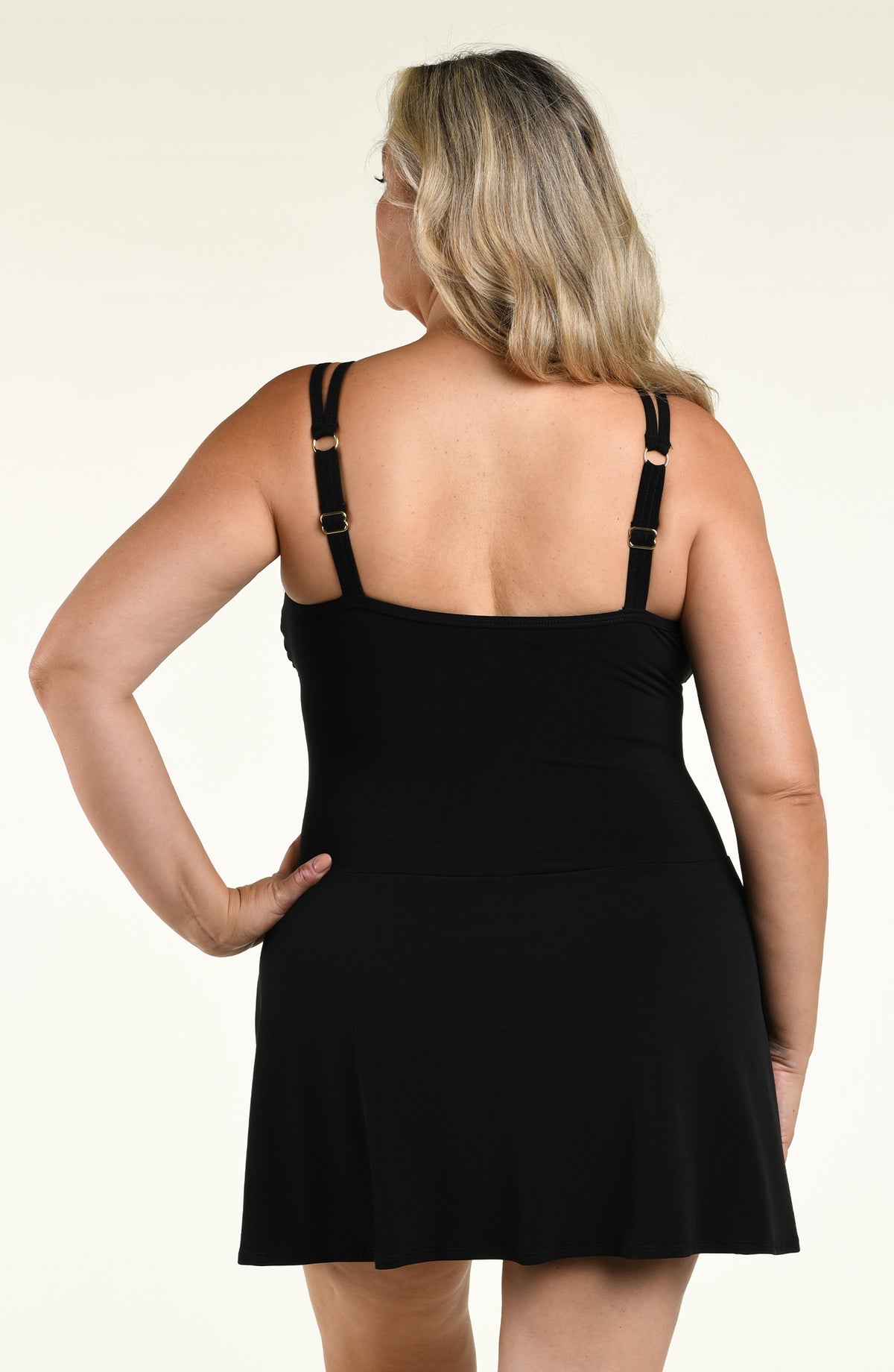 Woman wearing a solid black swim dress one piece swimsuit against a white background. 