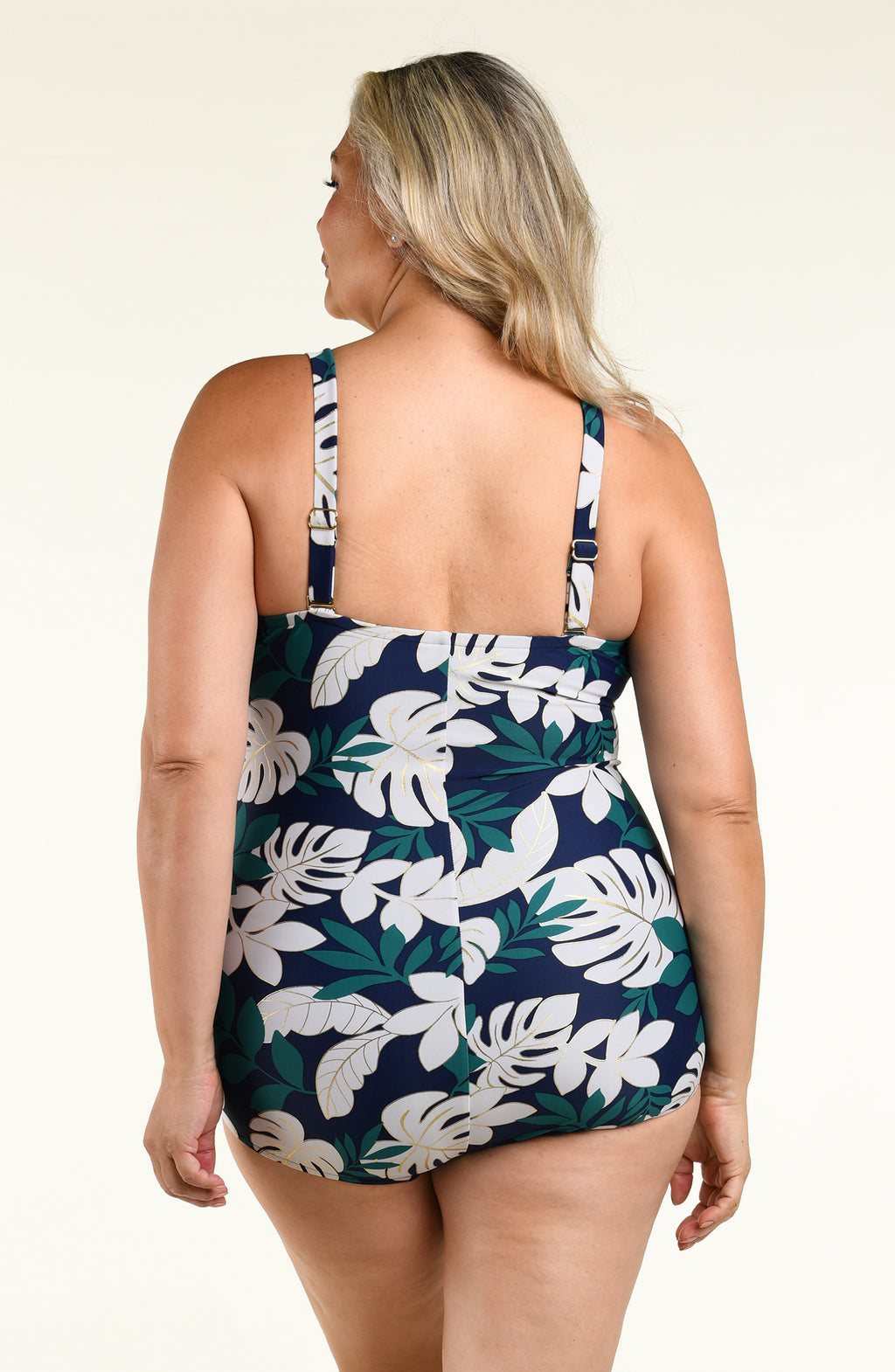 Woman wearing a green multicolored bandeau one piece swimsuit against a white background. 