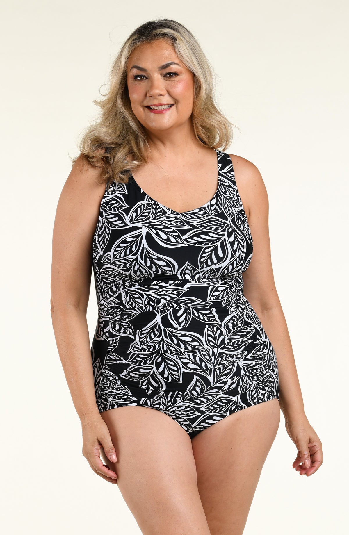 A woman modeling a one-piece swimsuit with a black and white tropical leaf pattern against a plain white studio background.