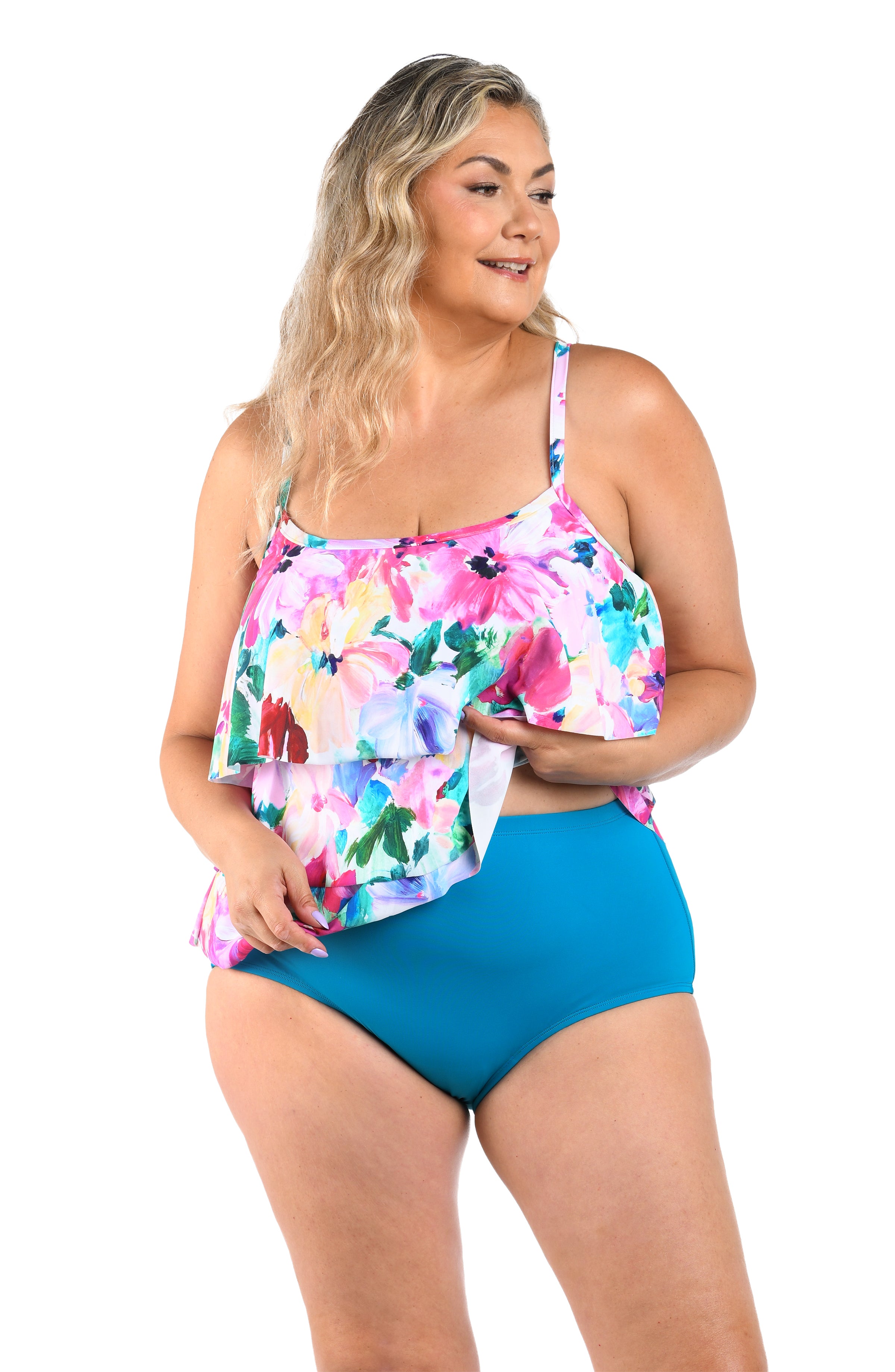 Woman wearing a colorful floral top and emerald colored high-waisted swimsuit bottoms on a white background