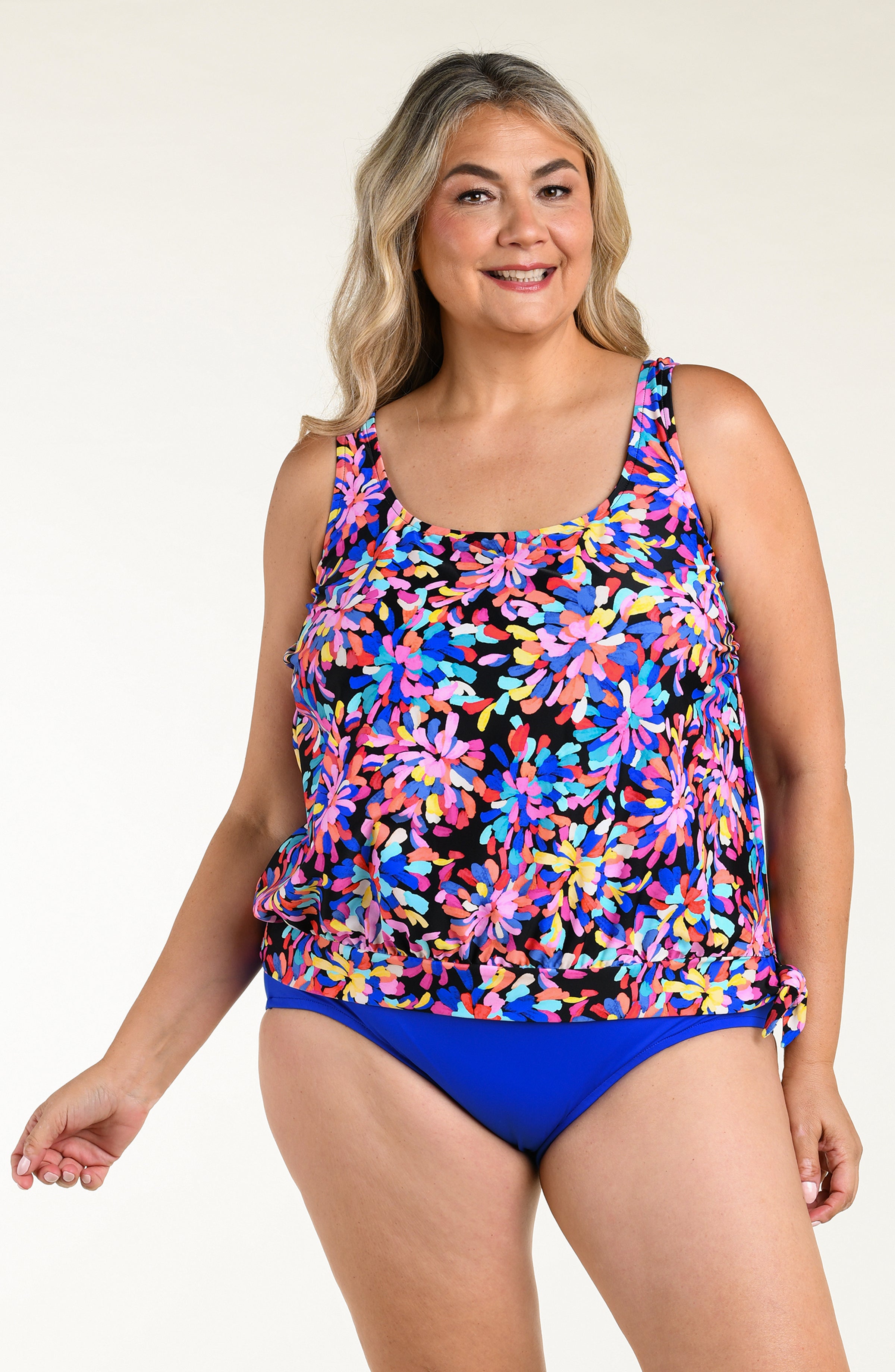 Woman wearing a colorful floral tankini top and blue bottom against a white background.