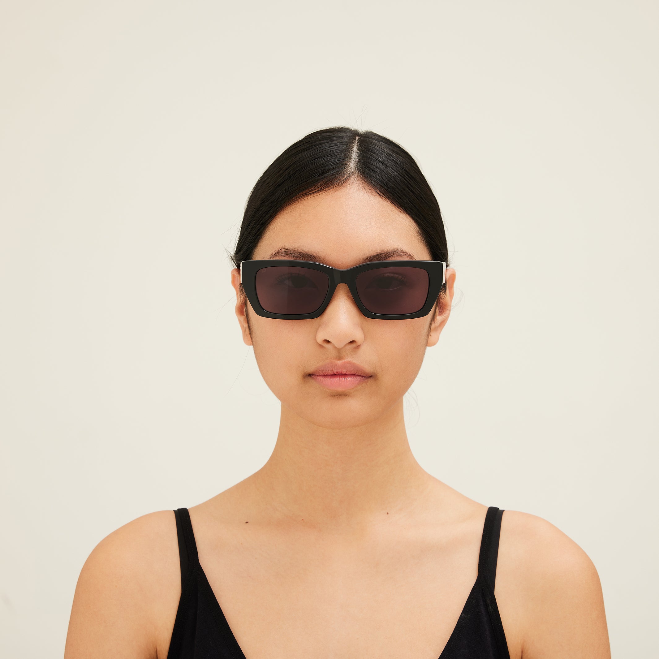Woman wearing dark sunglasses against a plain background