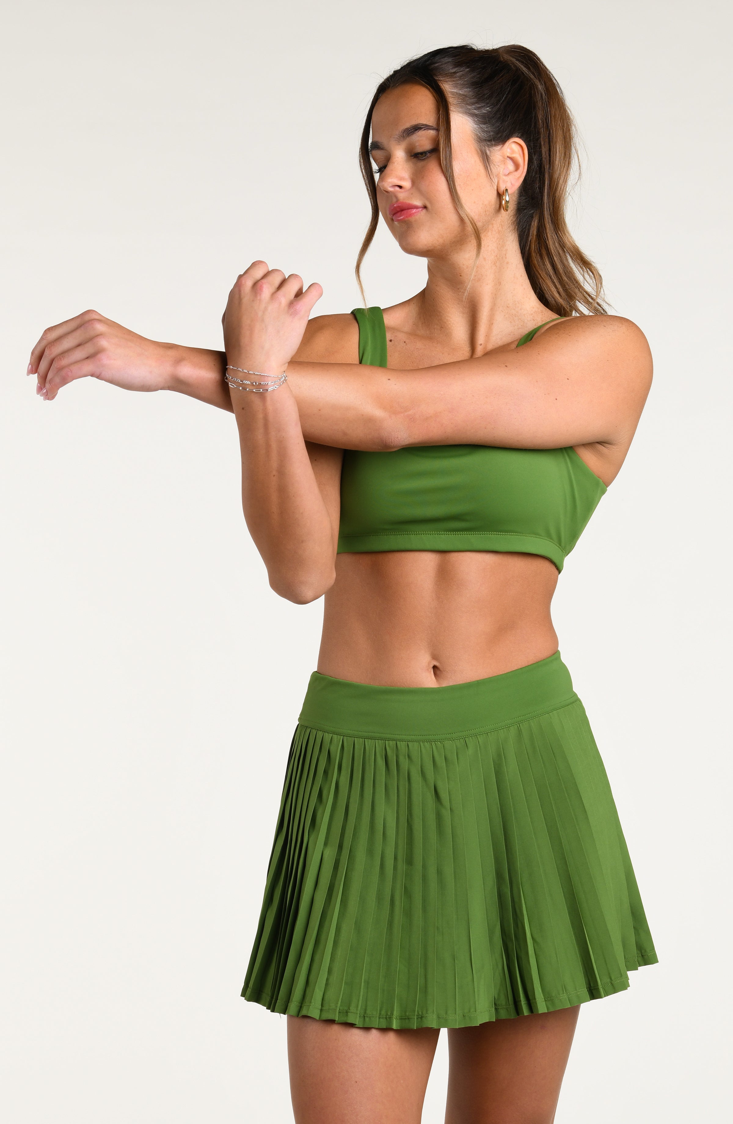 Woman wearing a green sports bra and matching swim skort against a white background