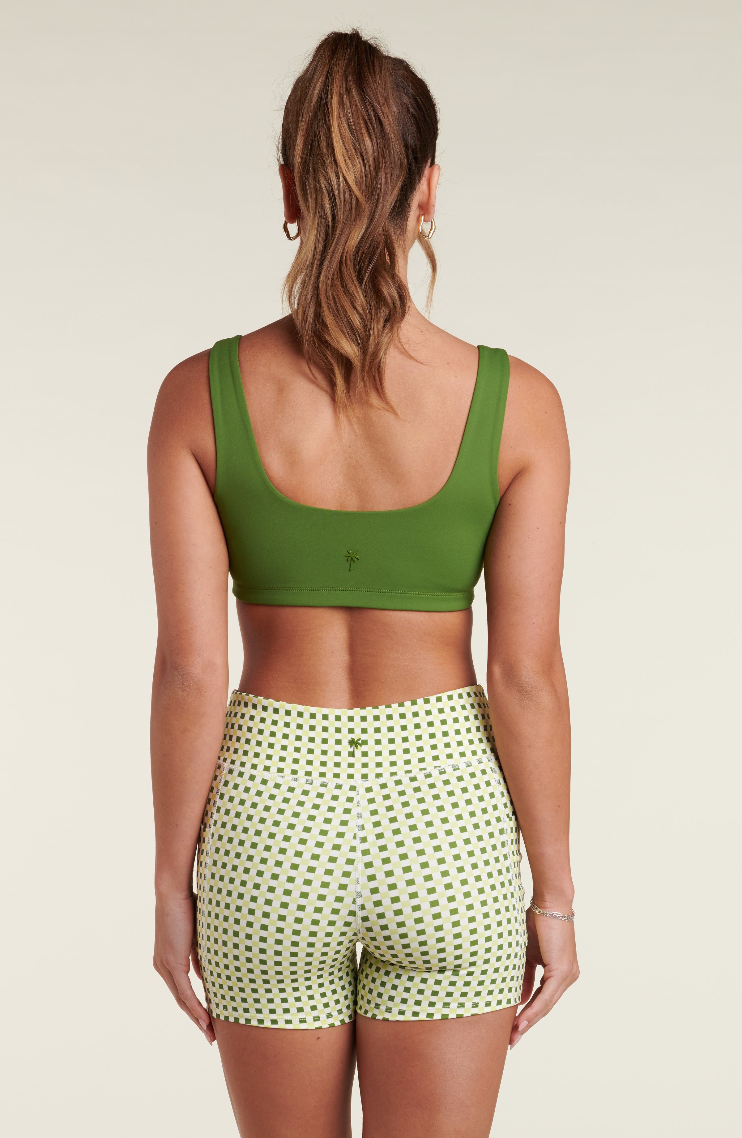 Woman wearing a green sports bra and a green and white multicolored bike short against a white background.