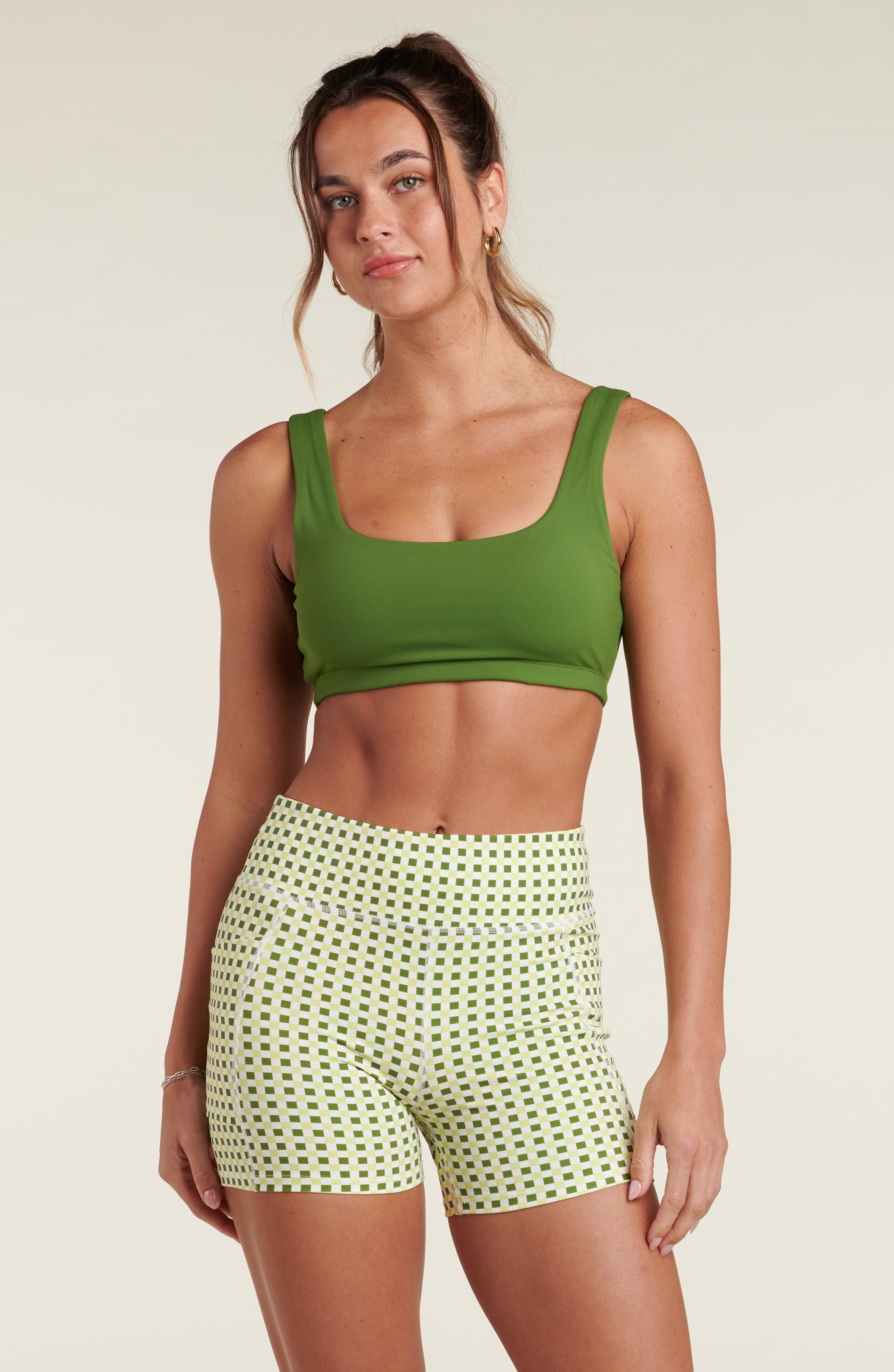 Woman wearing a green sports bra and a green and white multicolored bike short against a white background.