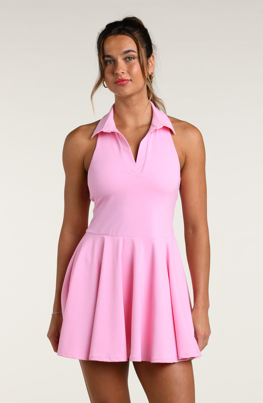 Woman wearing a light pink tennis dress against a white background.