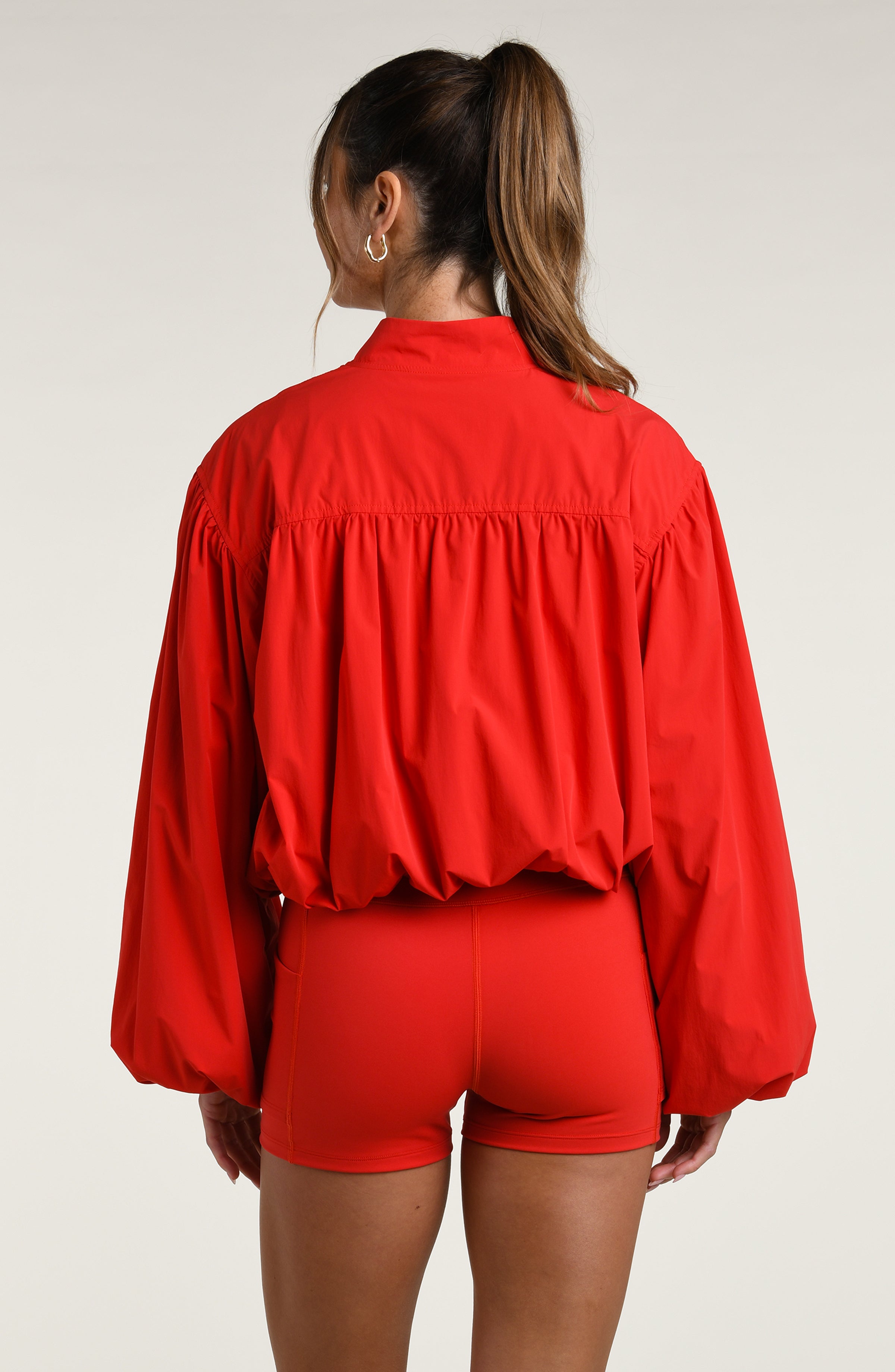 Woman wearing a red sports bra, biker shorts, and jacket against a white background.