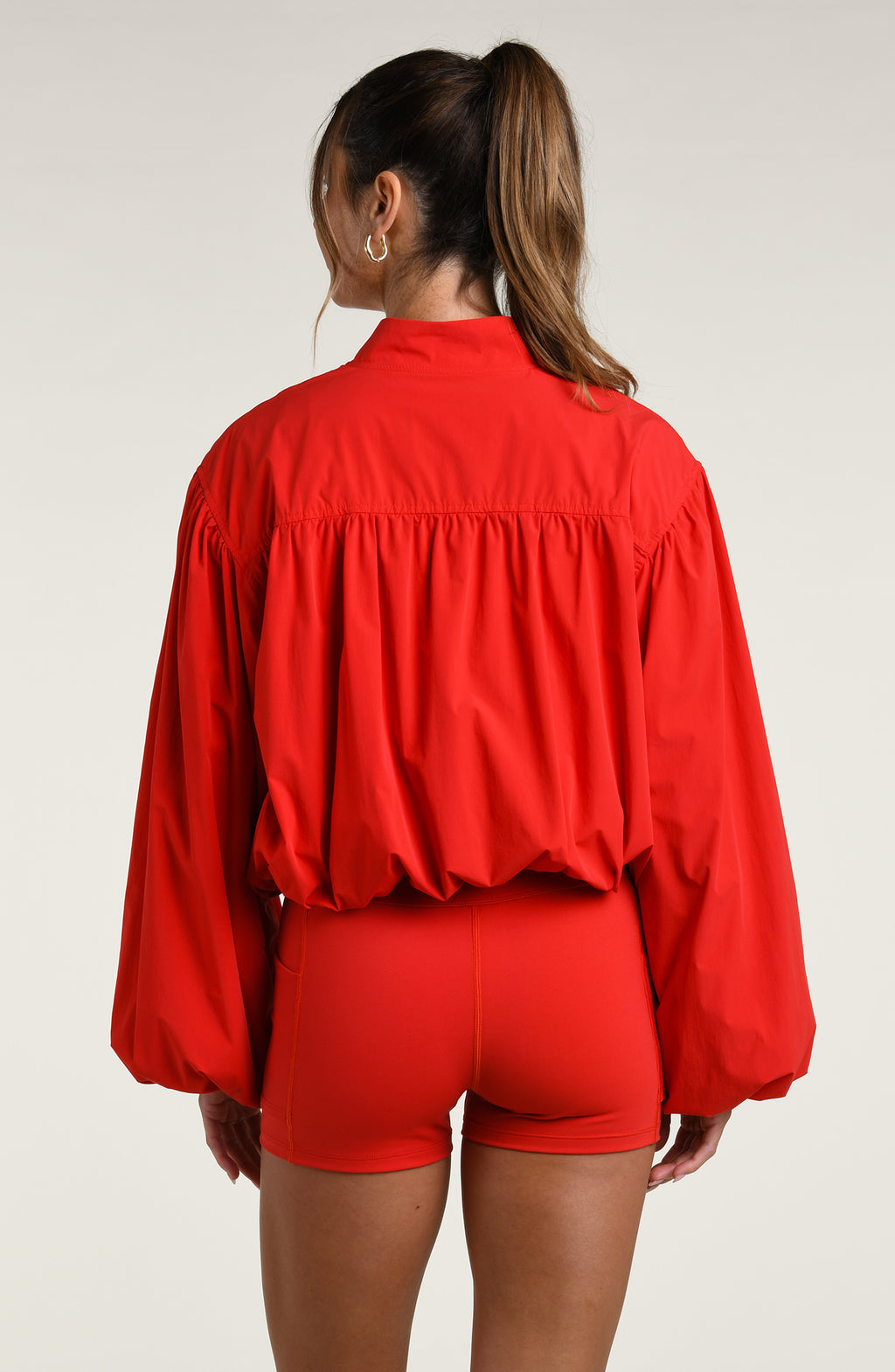 Woman wearing a red sports bra, biker shorts, and jacket against a white background.