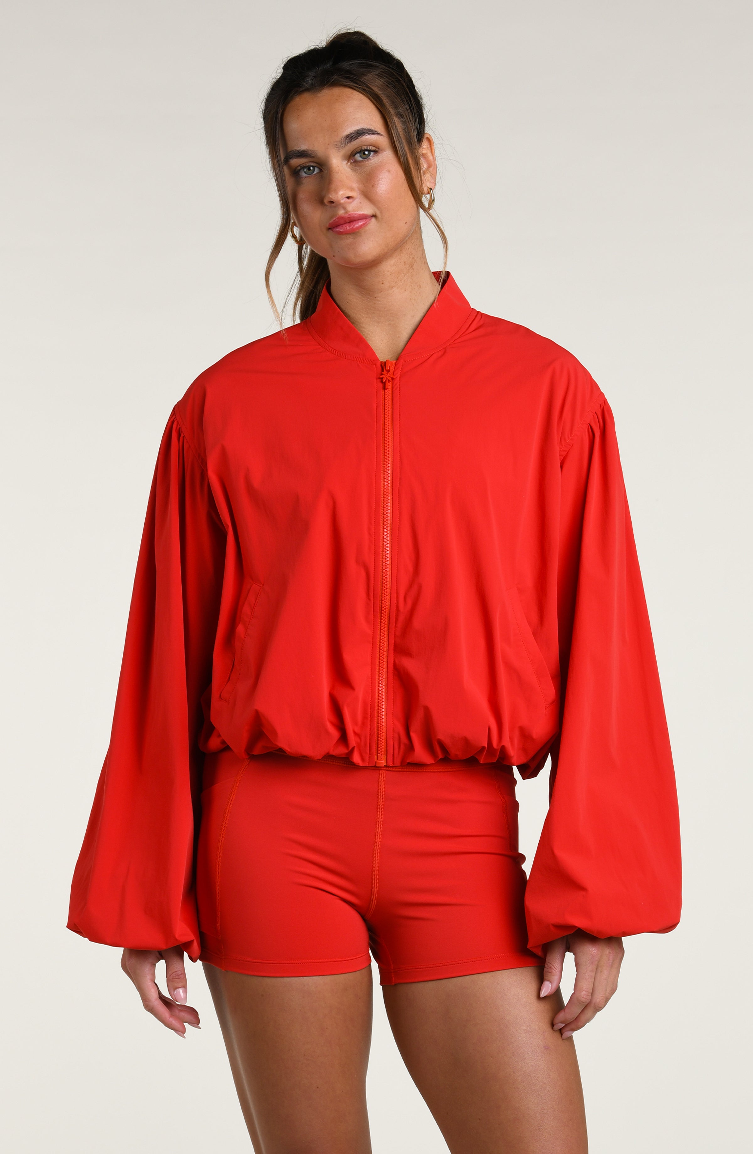 Woman wearing a red sports bra, biker shorts, and jacket against a white background.