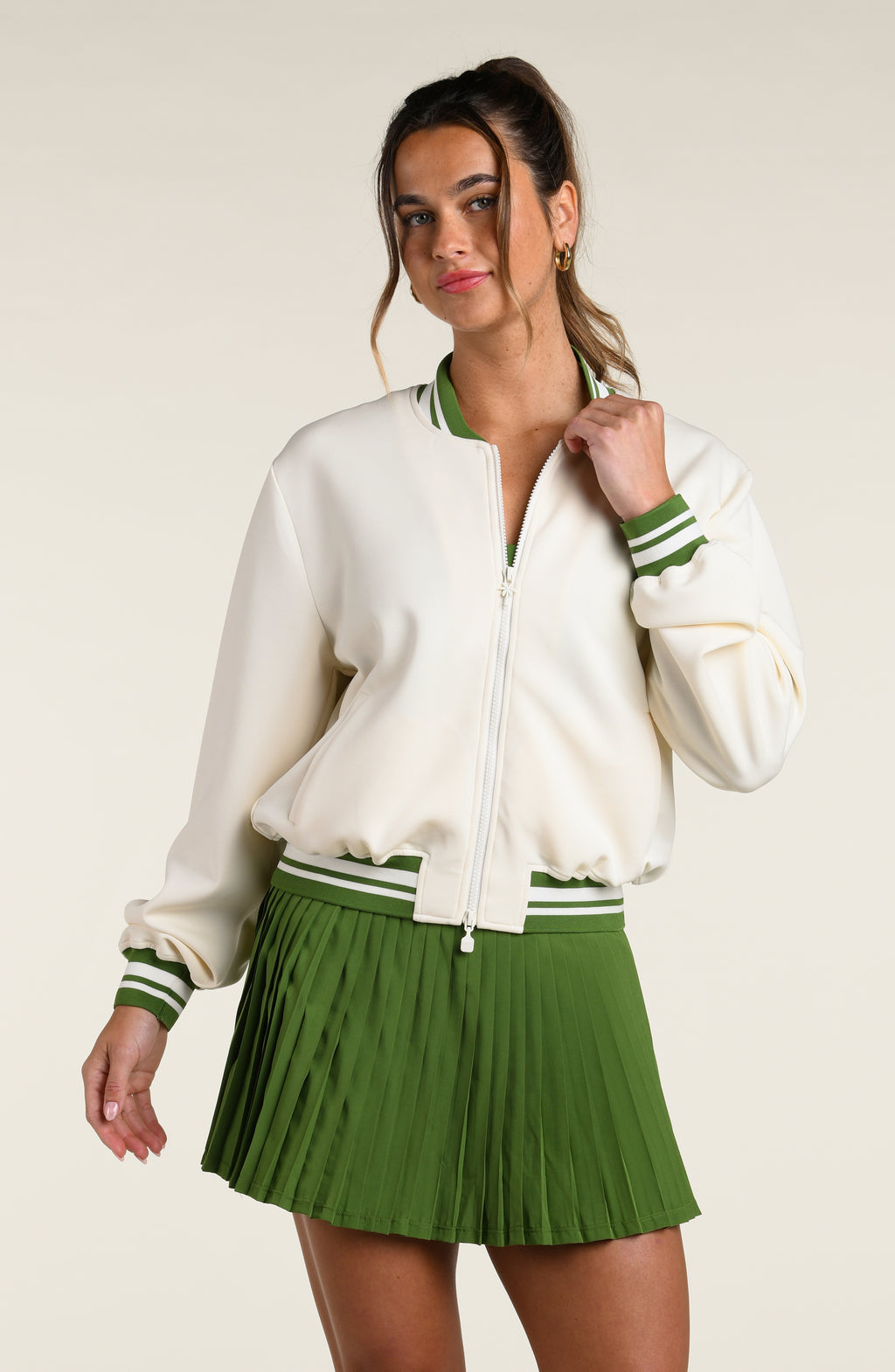Woman wearing a green sports bra, matching skort and white jacket with a palm tree logo, against a white background