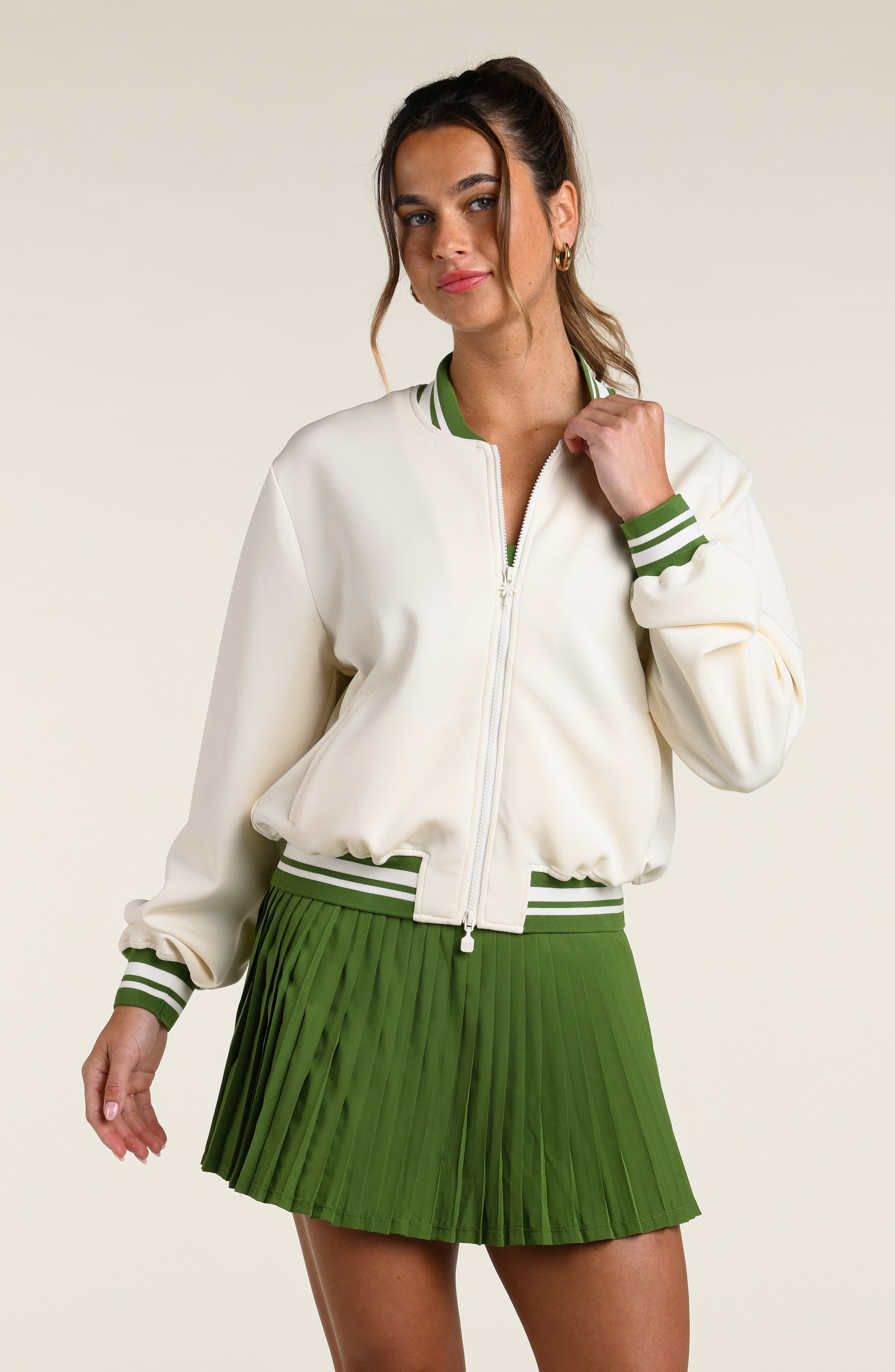 Woman wearing a green sports bra, matching skort and white jacket with a palm tree logo, against a white background