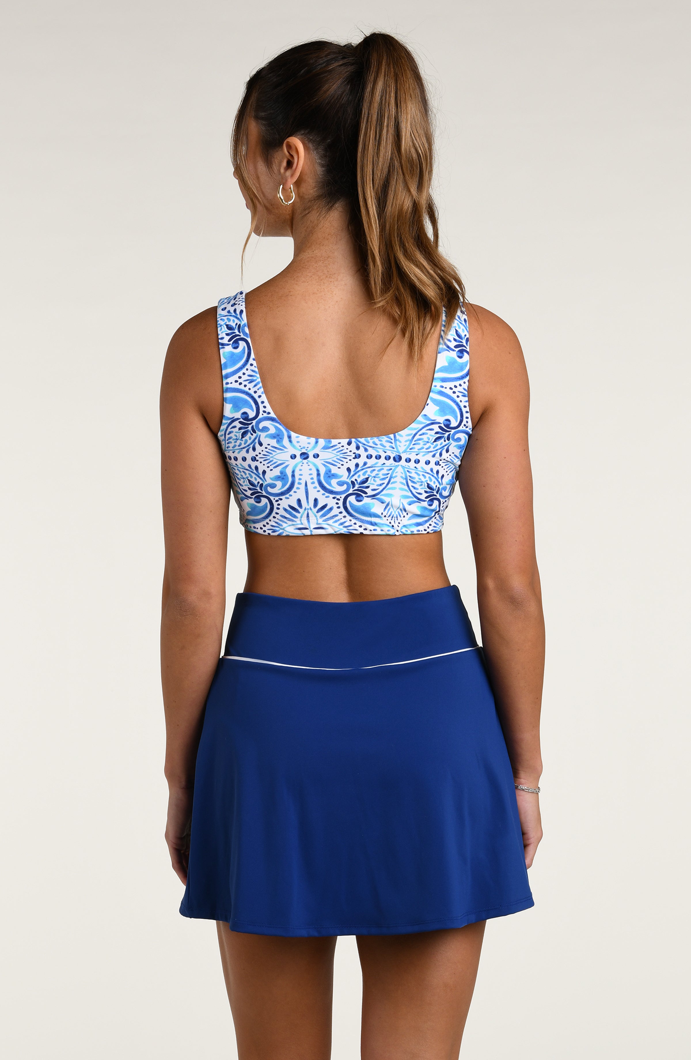 Woman wearing a blue and white patterned sports bra and blue active skorts against a white background