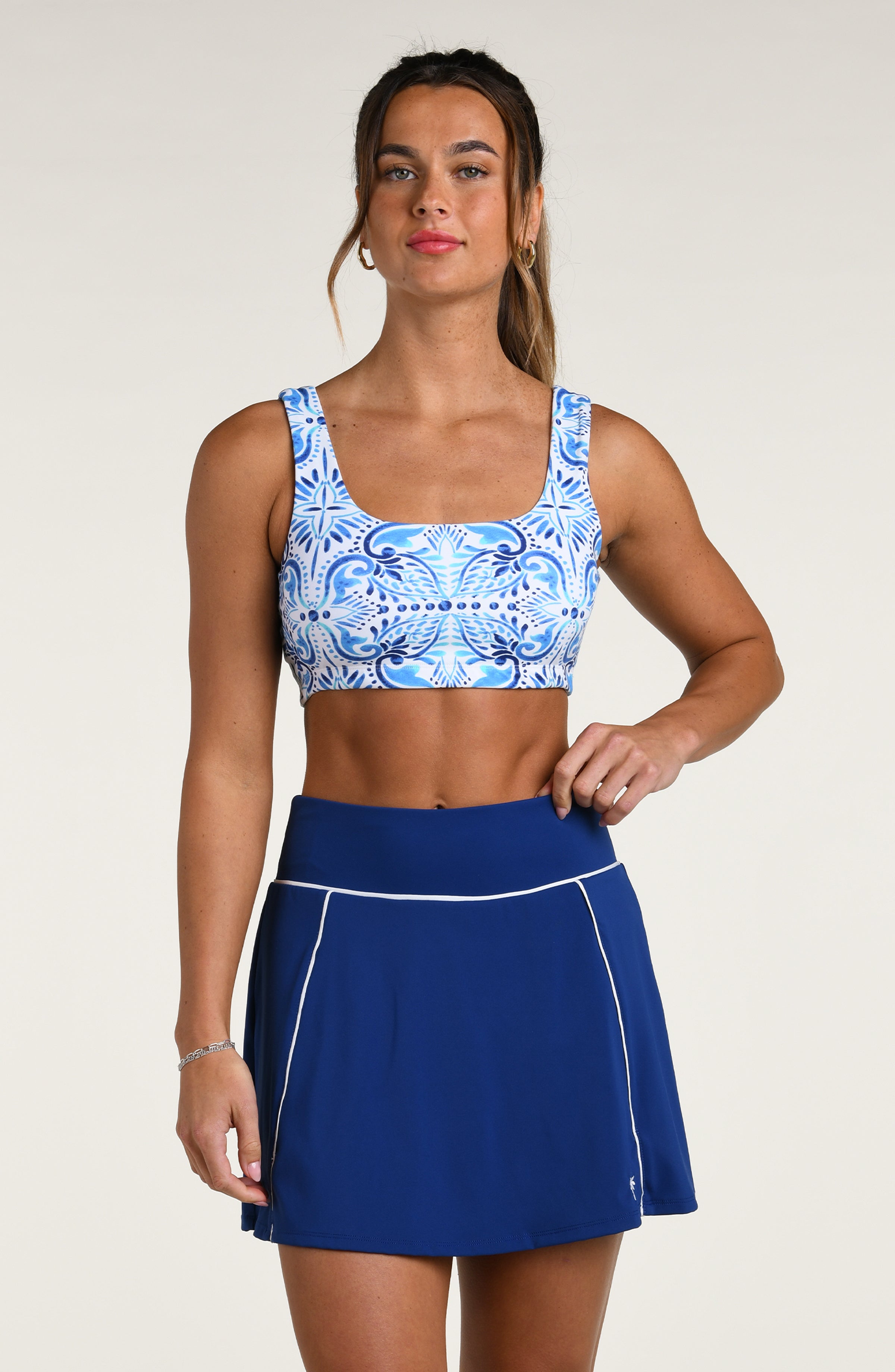 Woman wearing a blue and white patterned sports bra and blue active skorts against a white background