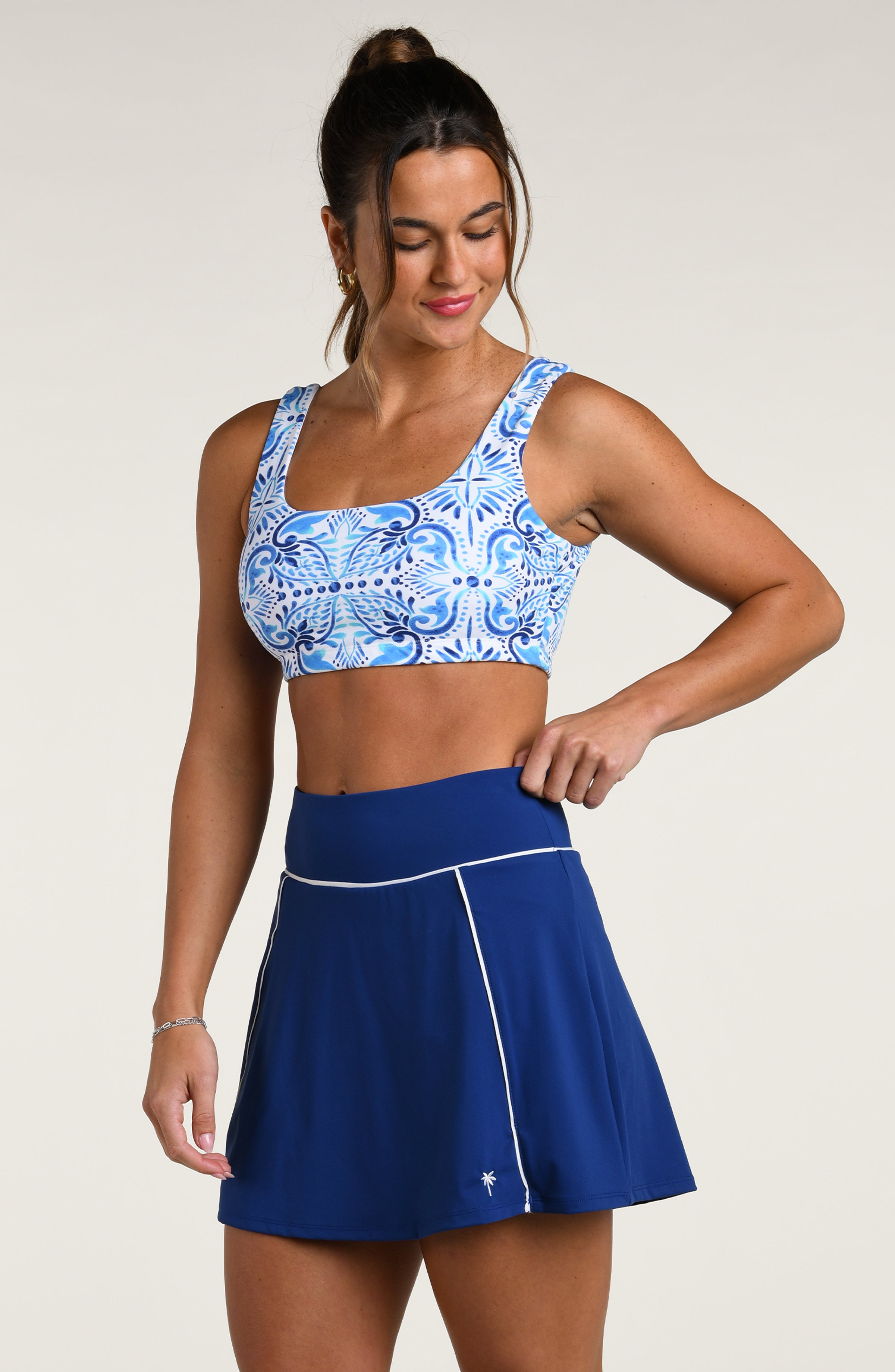 Woman wearing a blue and white patterned sports bra and dark blue active skort against a white background