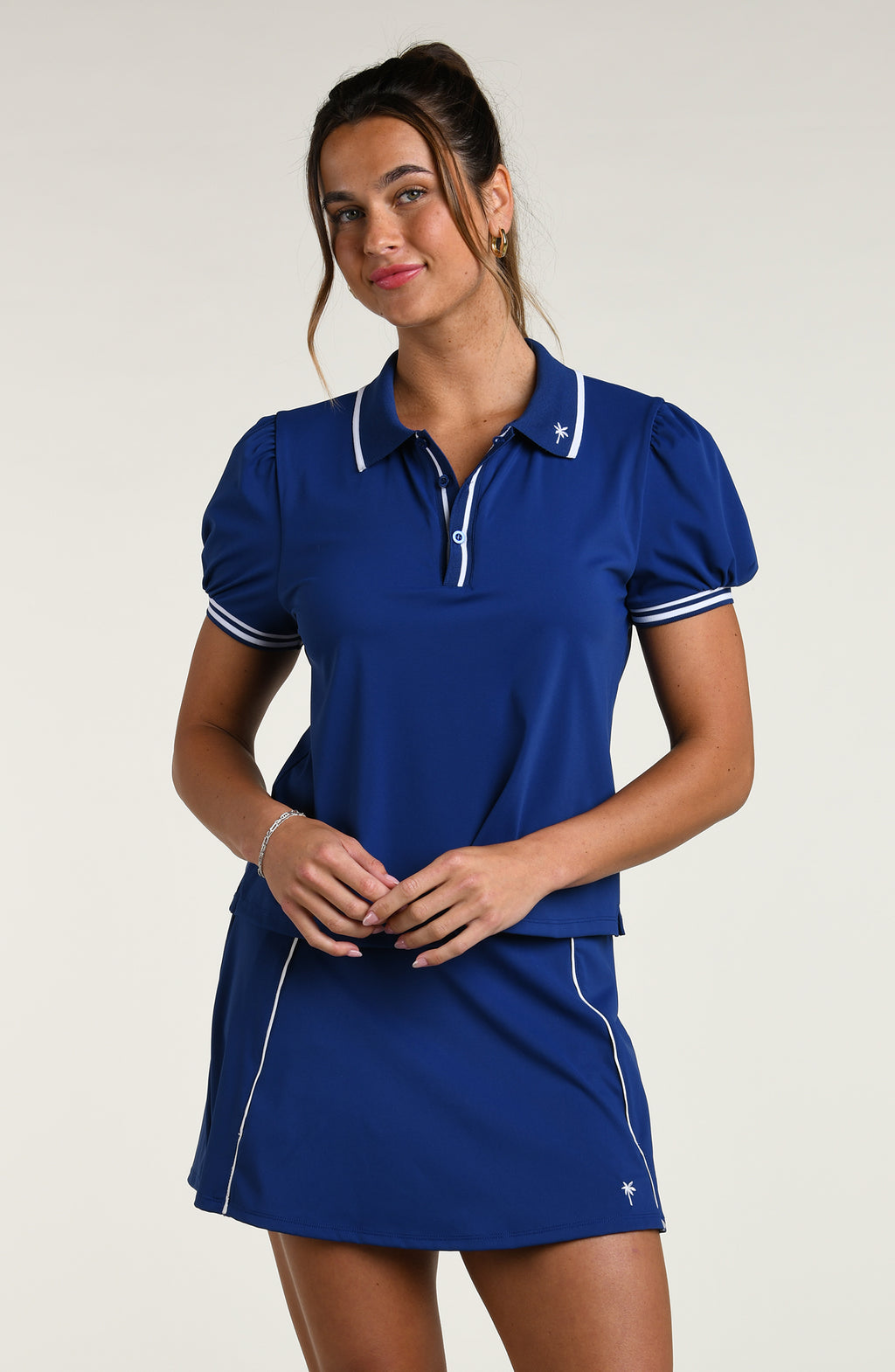 Woman wearing a blue polo shirt and skirt set against a white background