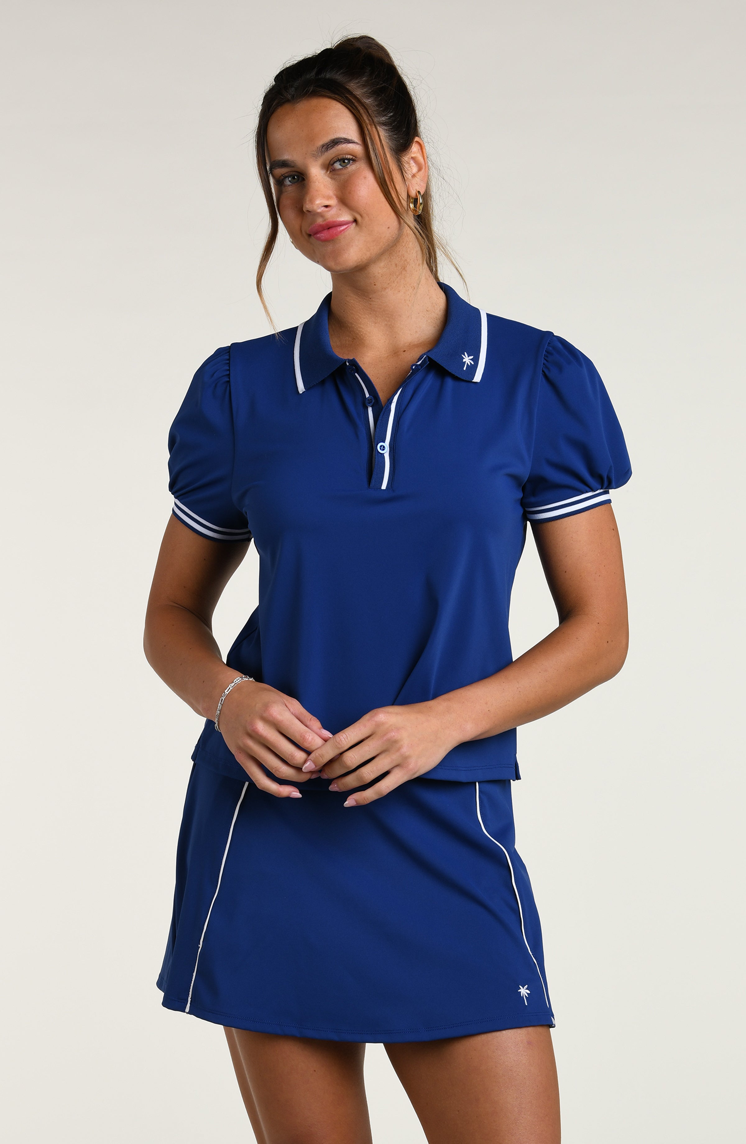 Woman wearing a blue polo shirt and skirt set against a white background