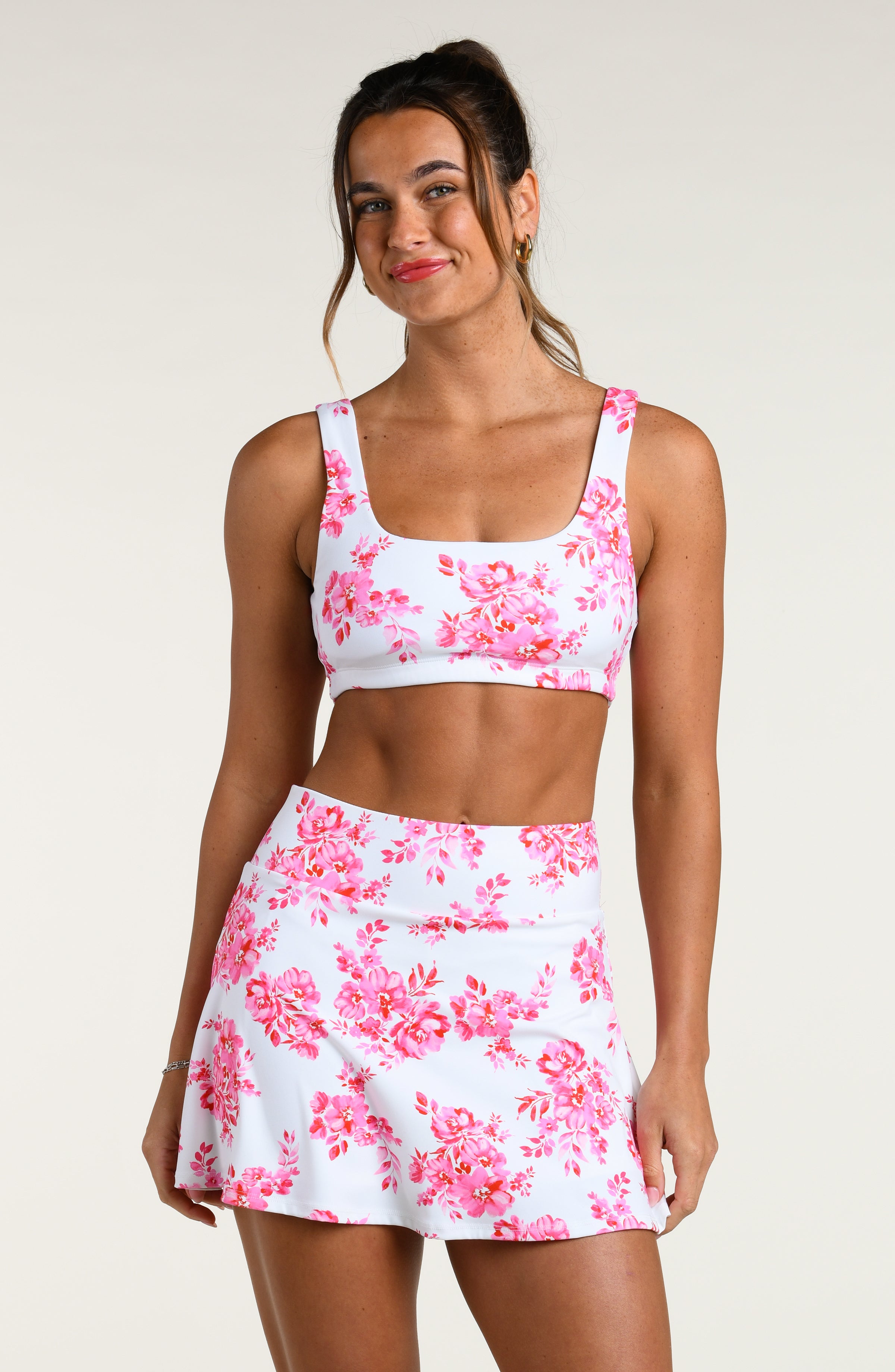 Woman wearing a pink floral sports bra and matching biker shorts set on a white background